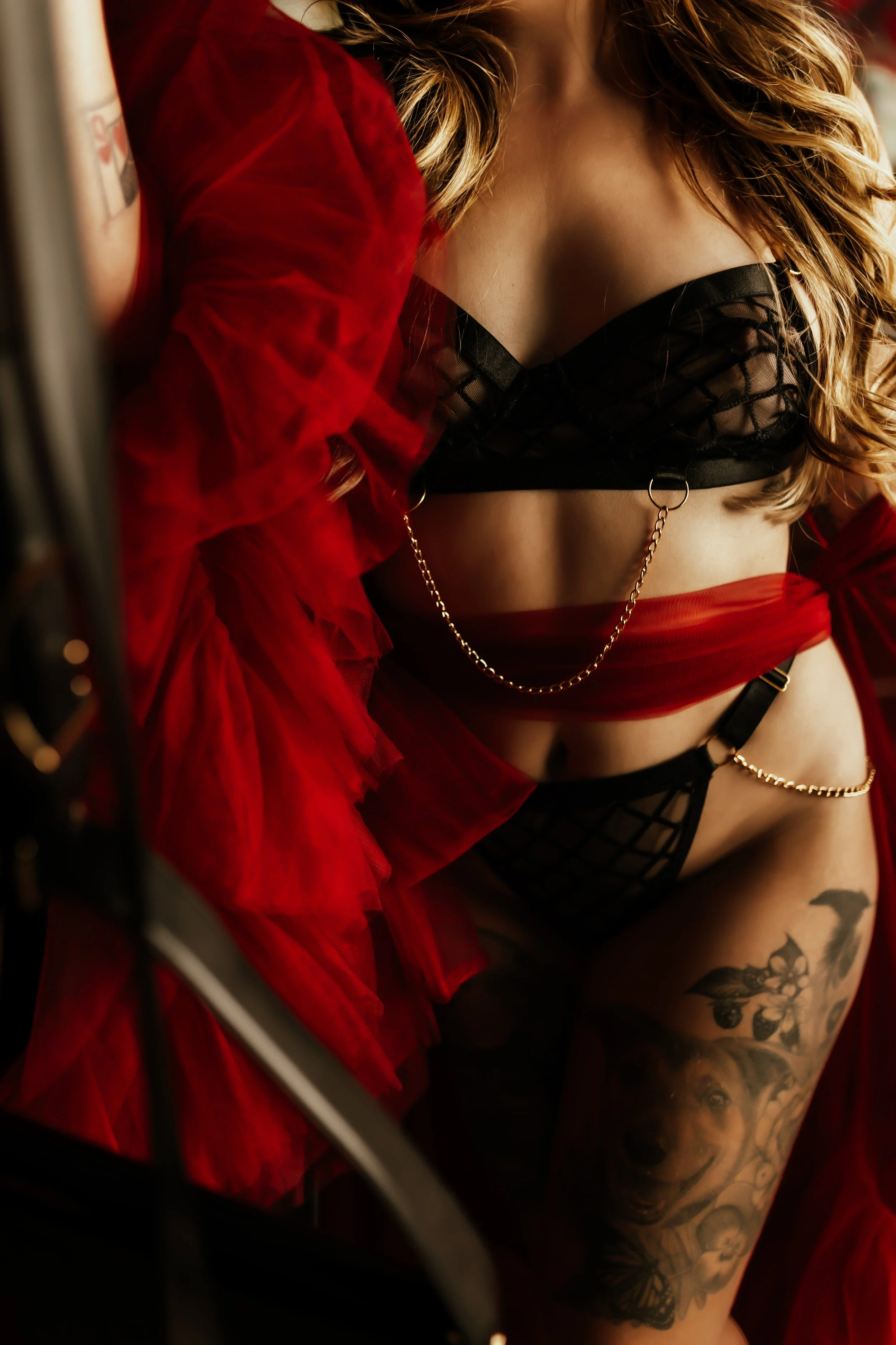 A woman wearing black lace lingerie and a red tulle skirt, with tattoos on her arm and thigh, is partially visible in the image.