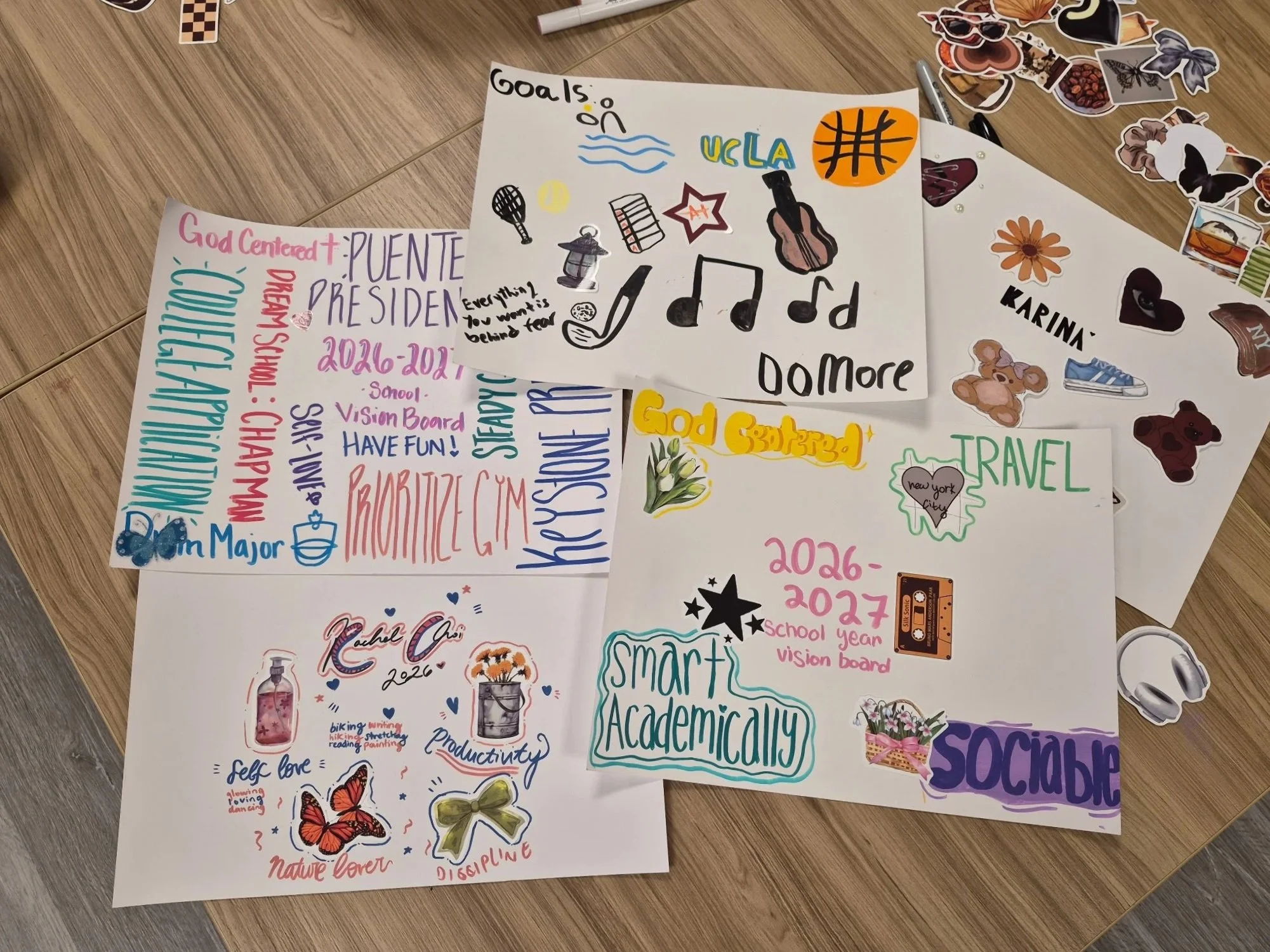 A table with colorful handwritten notes, stickers, and drawings related to school goals, activities, and personal interests. The notes include words like 'Goals', 'Travel', 'Smart Academic,' and 'Self Love,' along with doodles such as butterflies, flowers, and music notes.