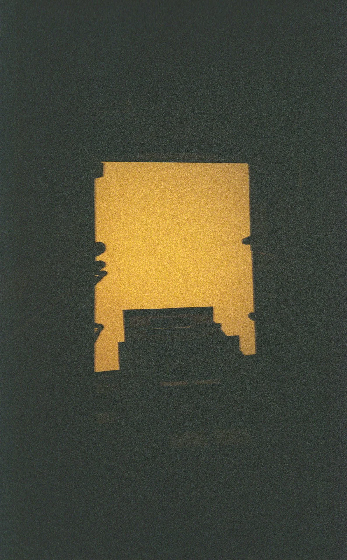 Silhouette of a person reaching up to touch a rectangular light source in a dark room.