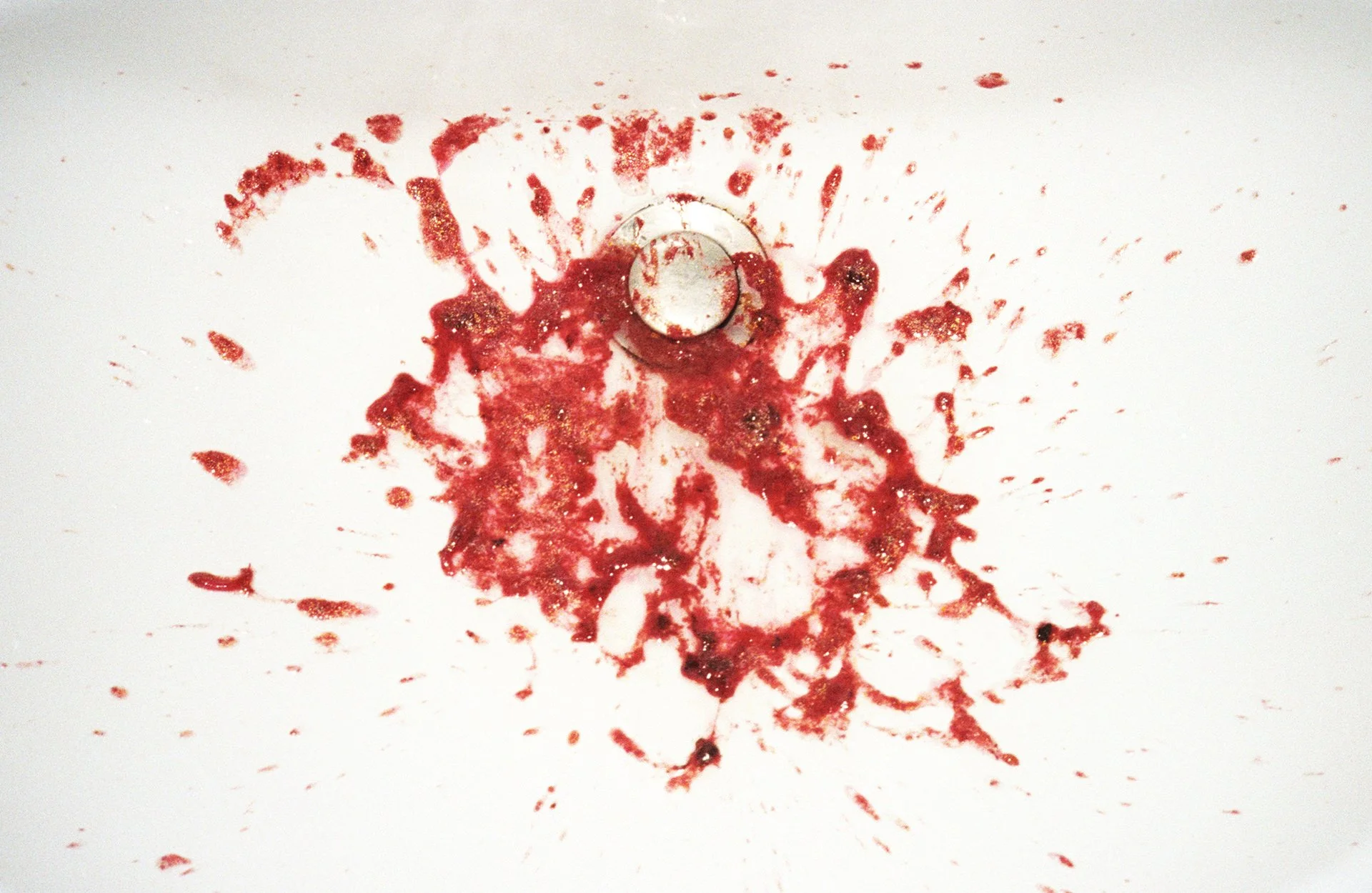 Blood splattered around a drain in a white surface.