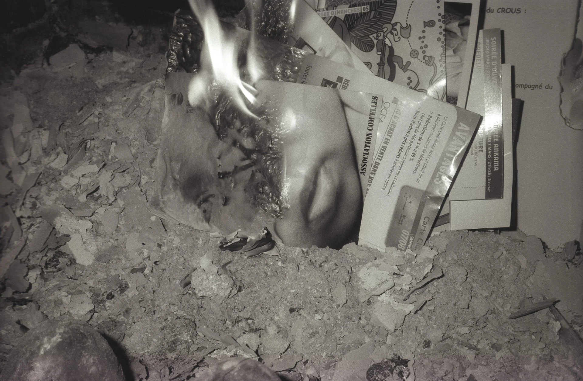 A close-up of a pile of ash, debris, and crumpled papers burning with visible flames.