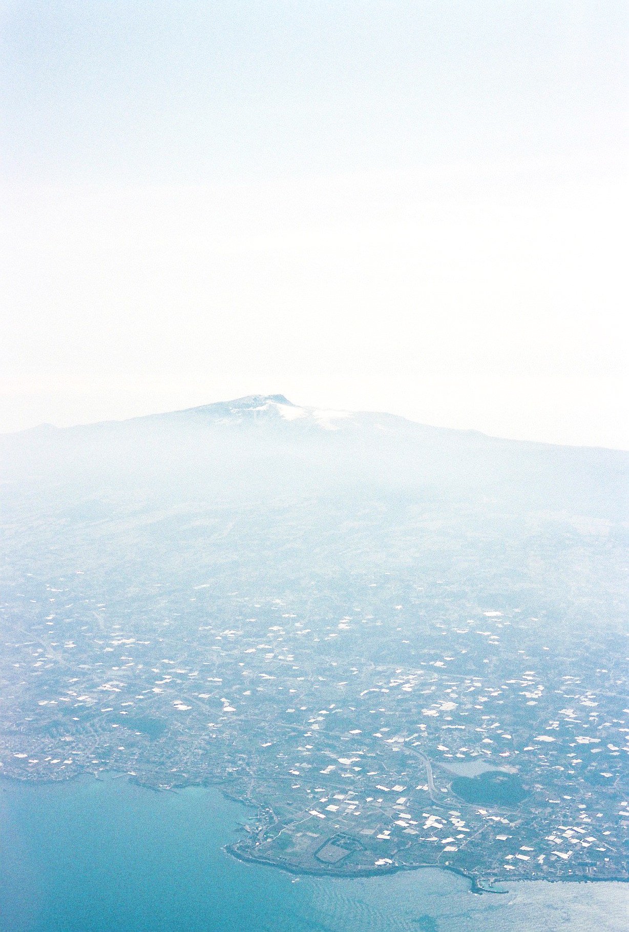 Aerial view of a volcanic island surrounded by water, with snow-capped mountain in the background.