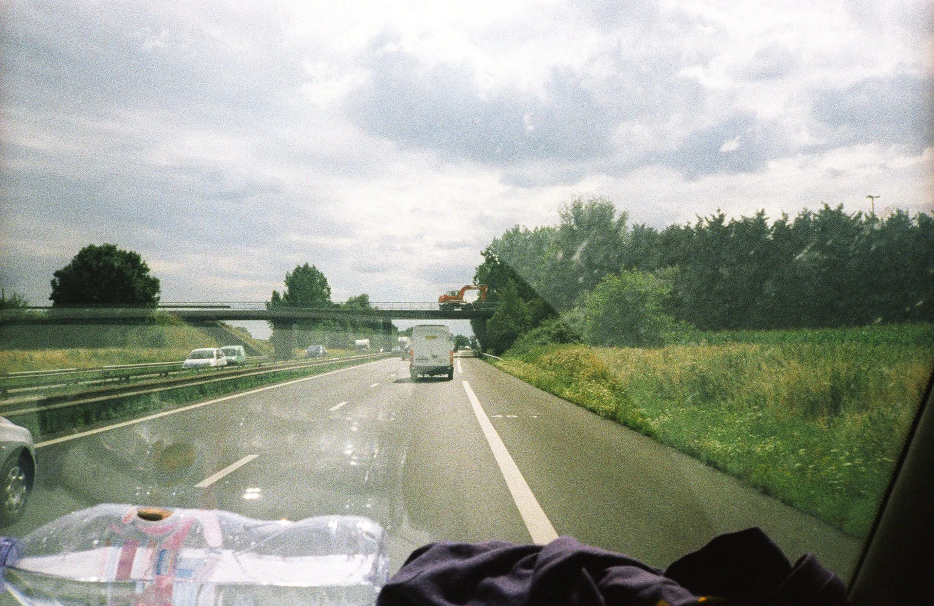 Photo taken from inside a car on a highway, showing other vehicles, trees, and an overpass with a construction vehicle on top.