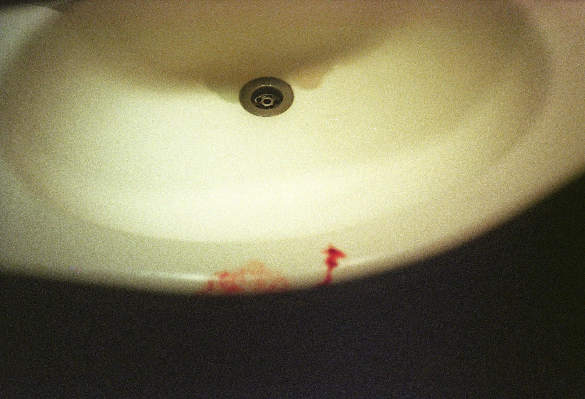 The interior of a white sink with a shiny drain in the center and some red spots near the edge.