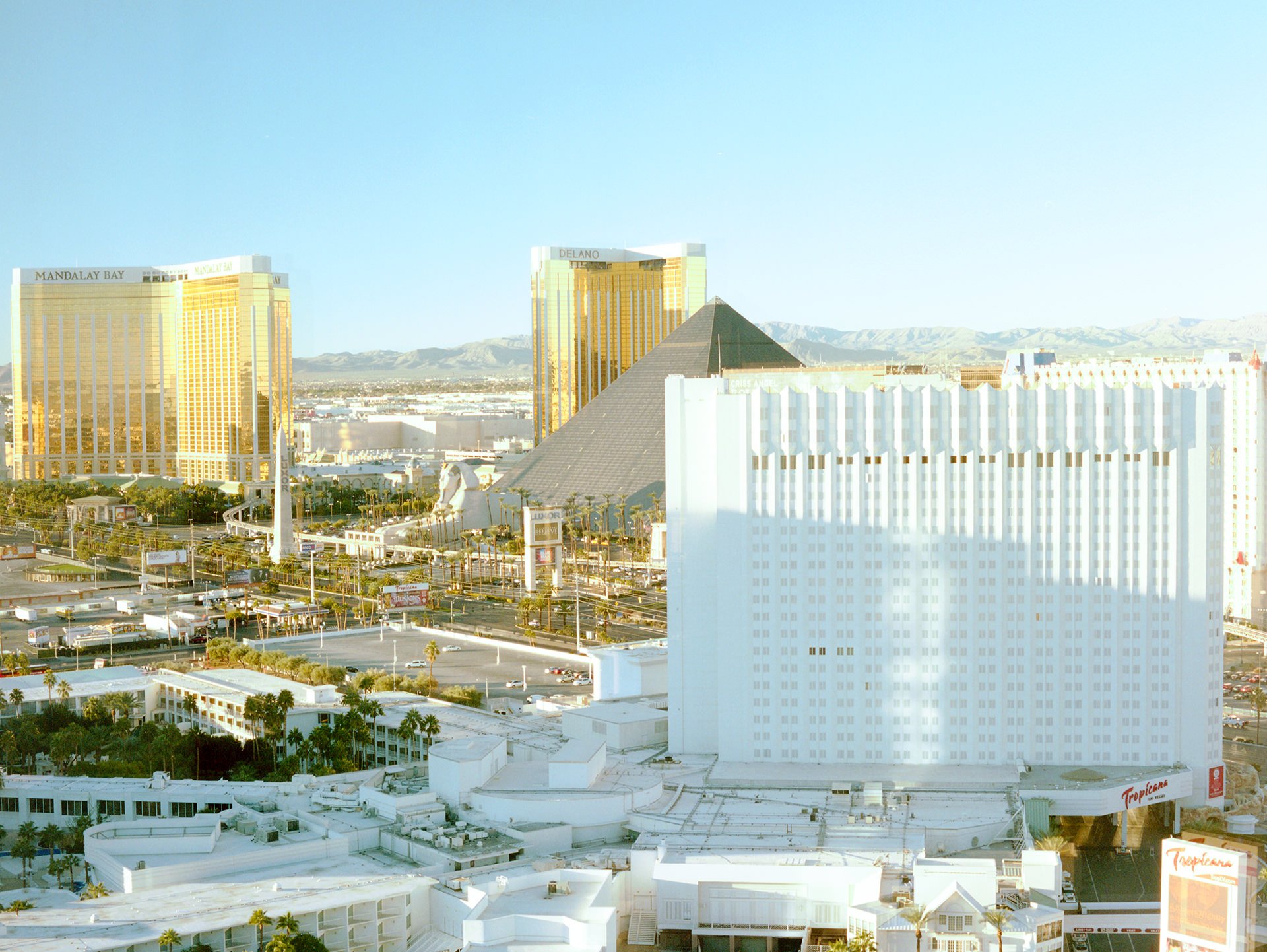 Cityscape view of Las Vegas with white buildings, golden hotels, and mountains in the background on a clear blue sky day.