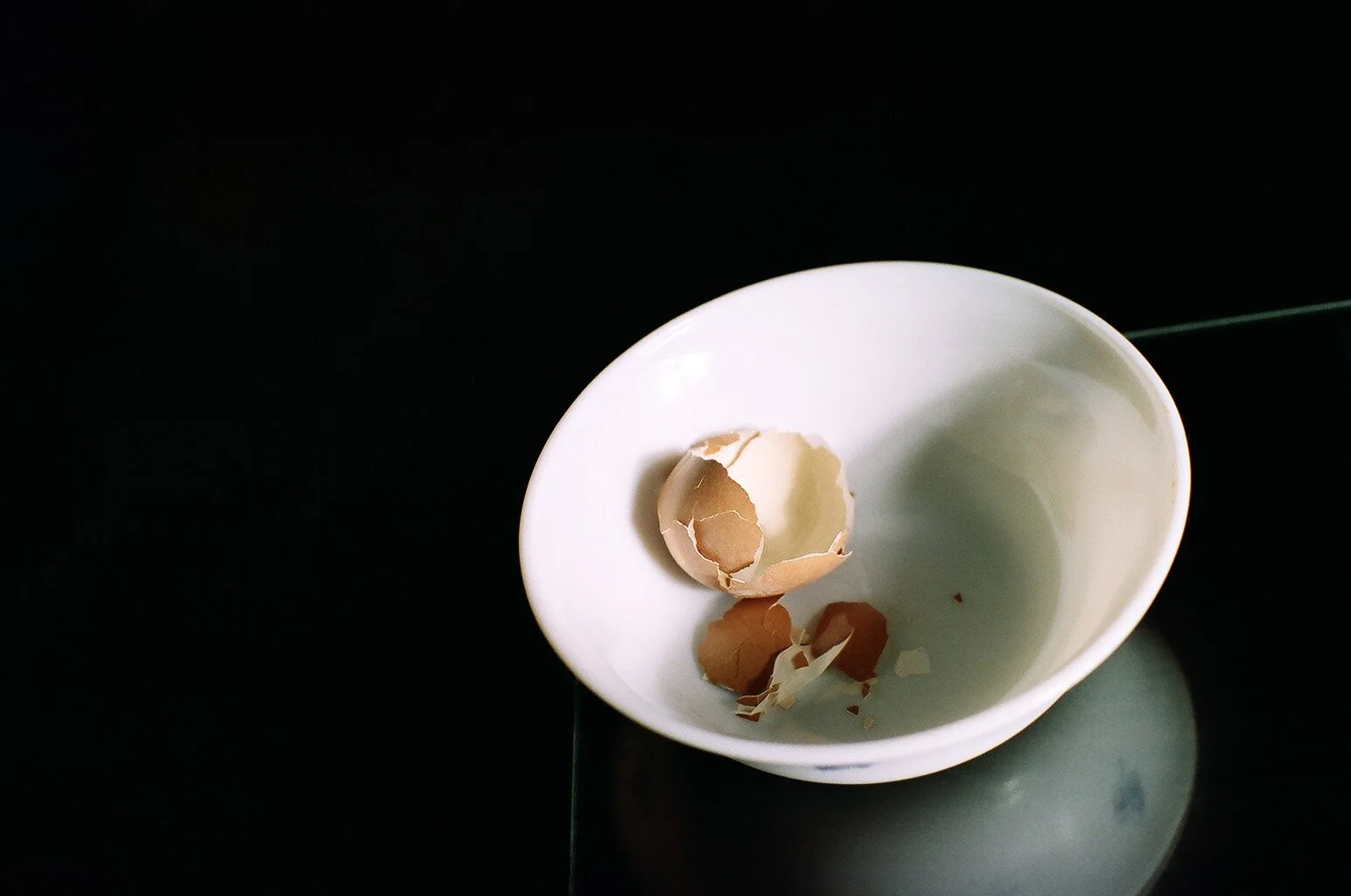 Empty eggshell in a white bowl on a dark surface.