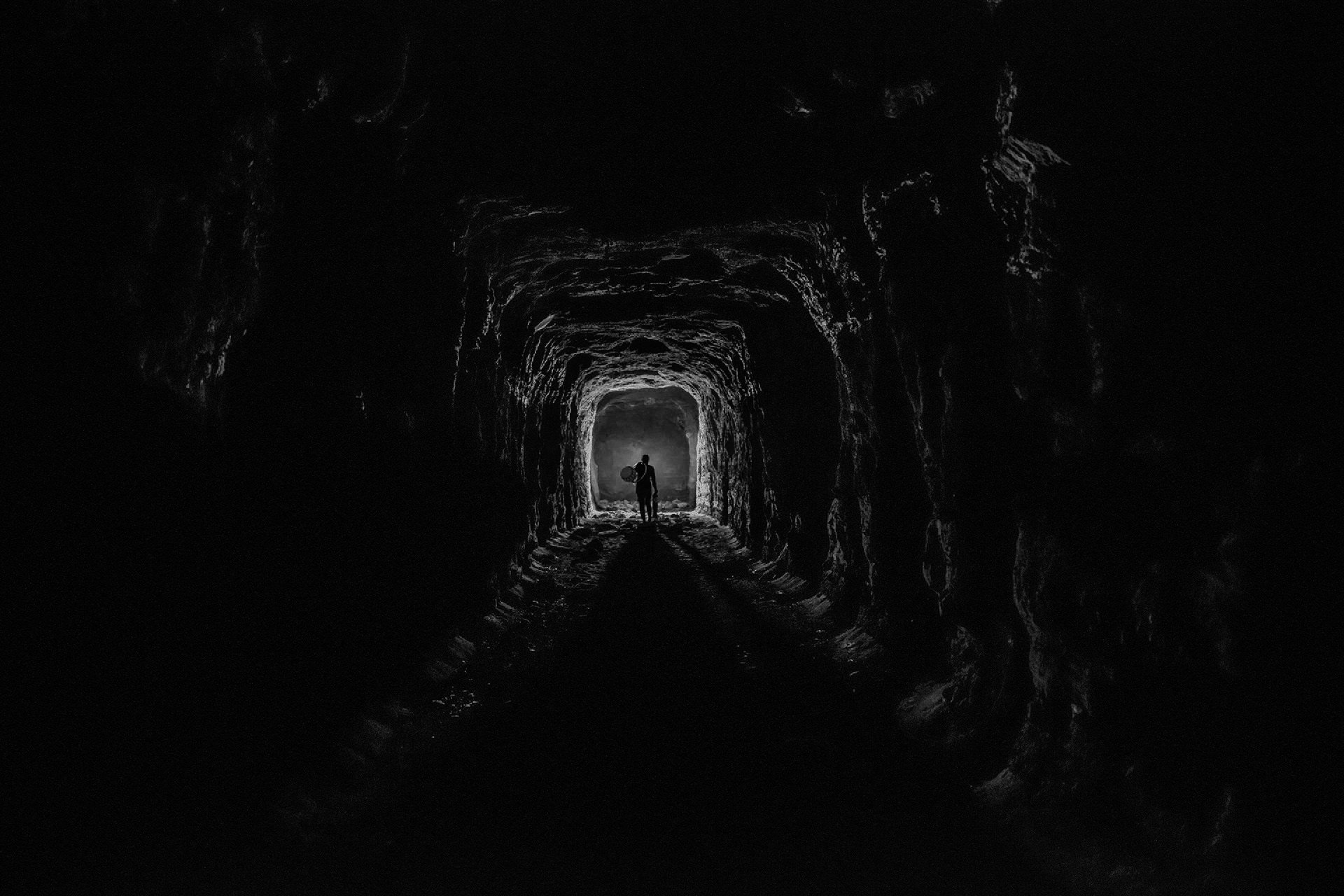 Silhouette of a person walking through a dark, tunnel-like cave with textured rocky walls.