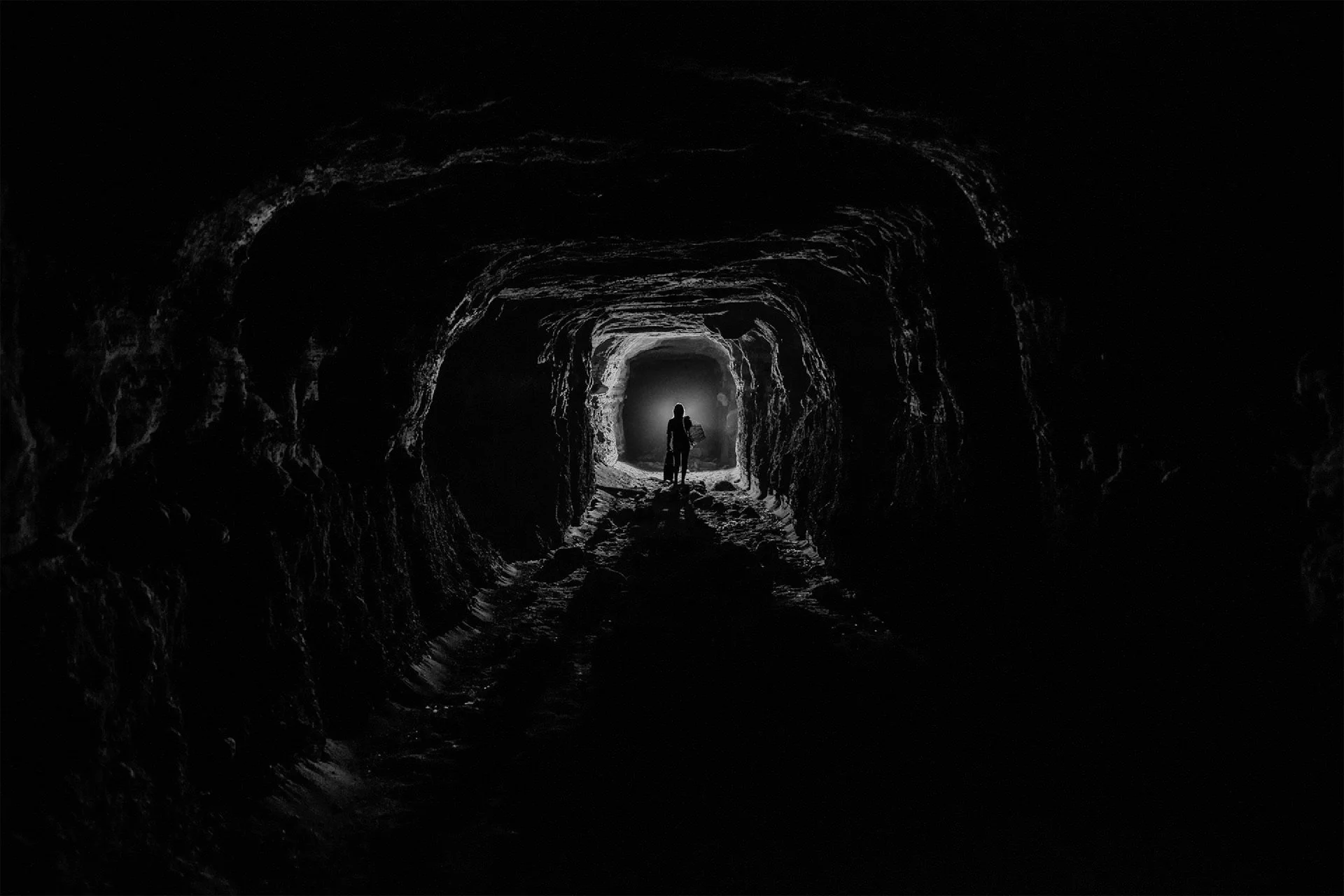 Silhouetted person walking inside a dark tunnel towards a light at the end.