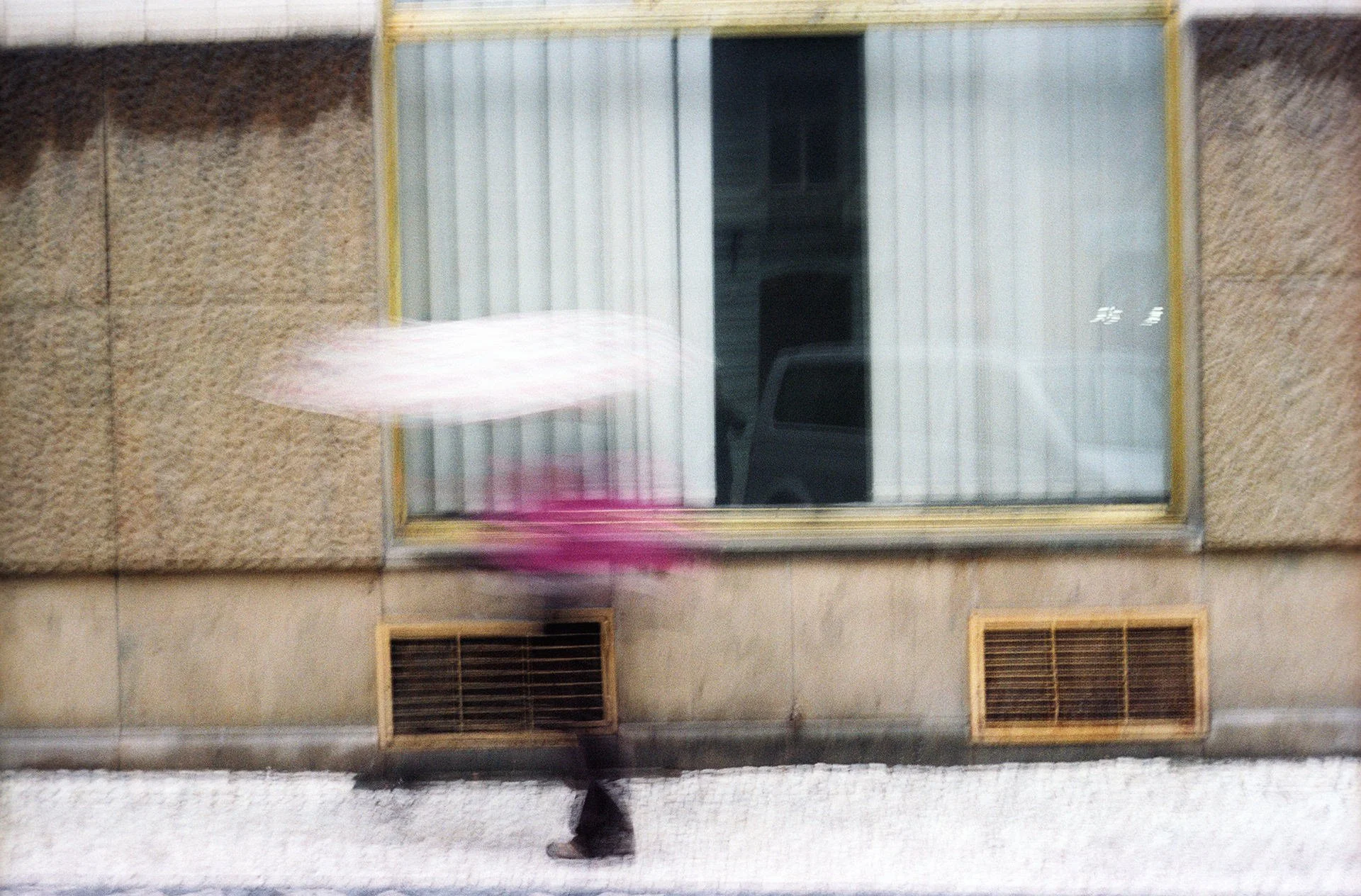 A person walking past a building with a window and vents visible on the exterior wall.