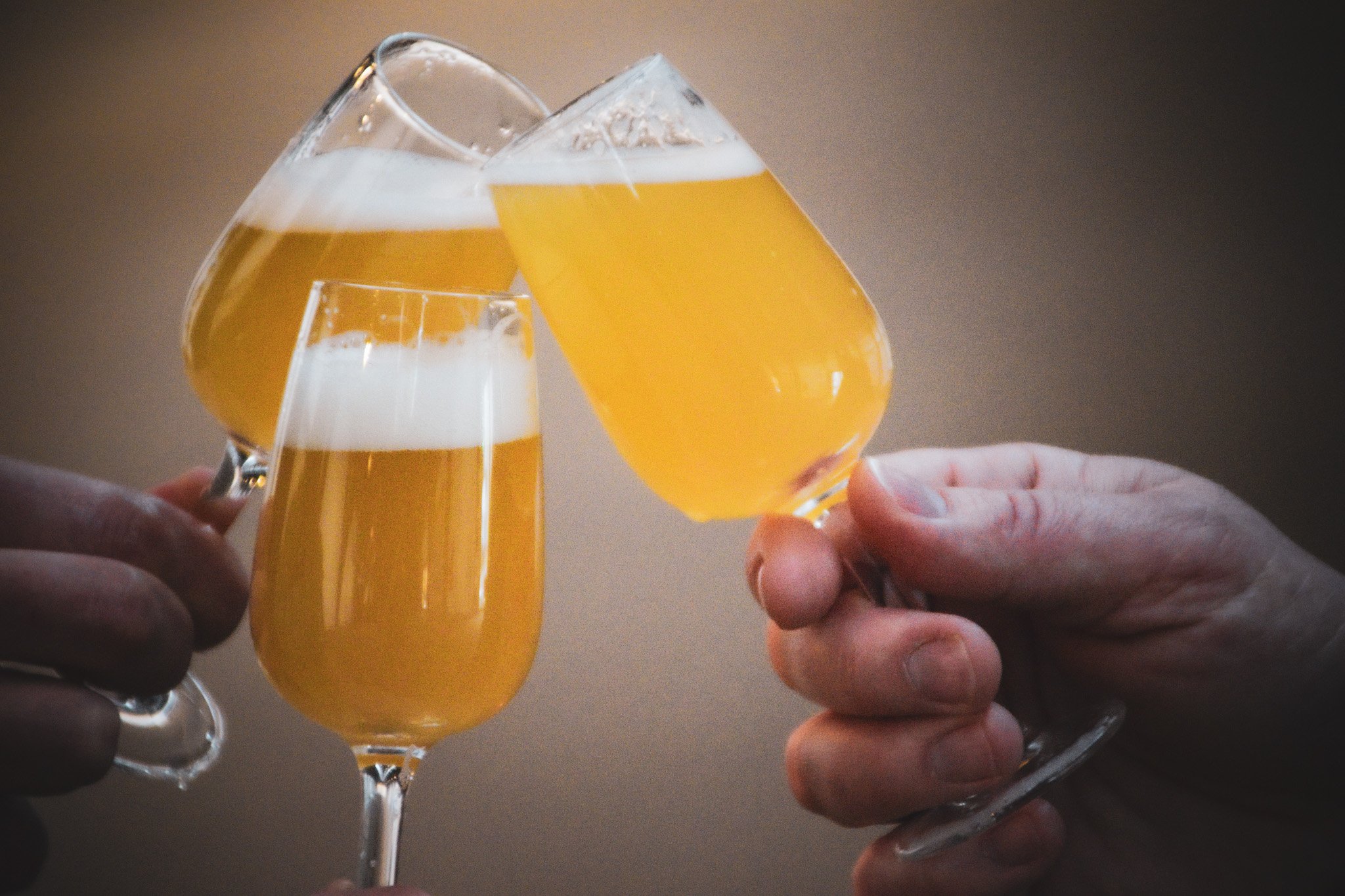 Tre personer, der skåler med små stilke-glas fyldt med øl.