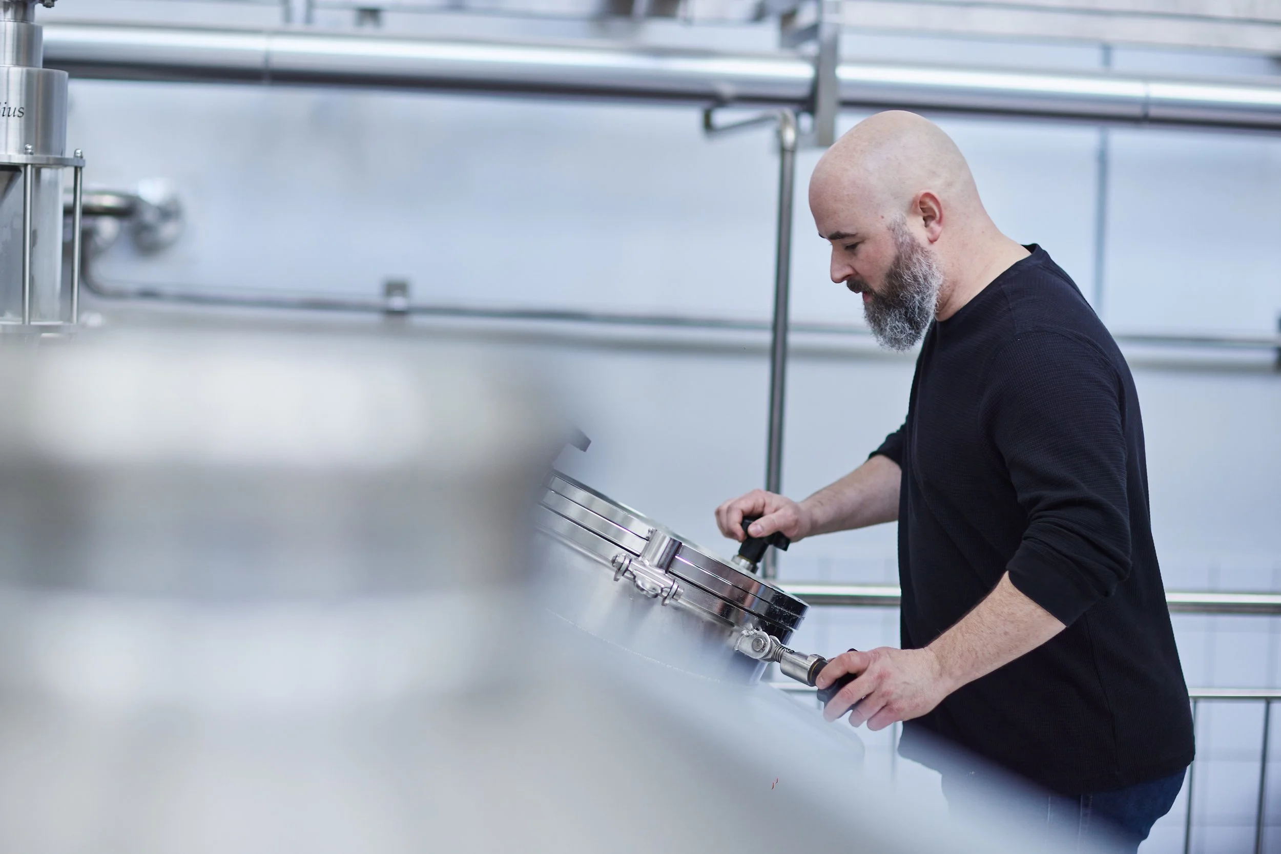 A man with a bald head and a gray beard working in a laboratory, examining a large metallic device or component.