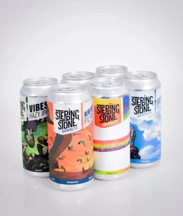 Six cans of craft beer from Stepping Stone Brewing Co., each with colorful label designs featuring nature scenes and vibrant colors, arranged on a white surface.