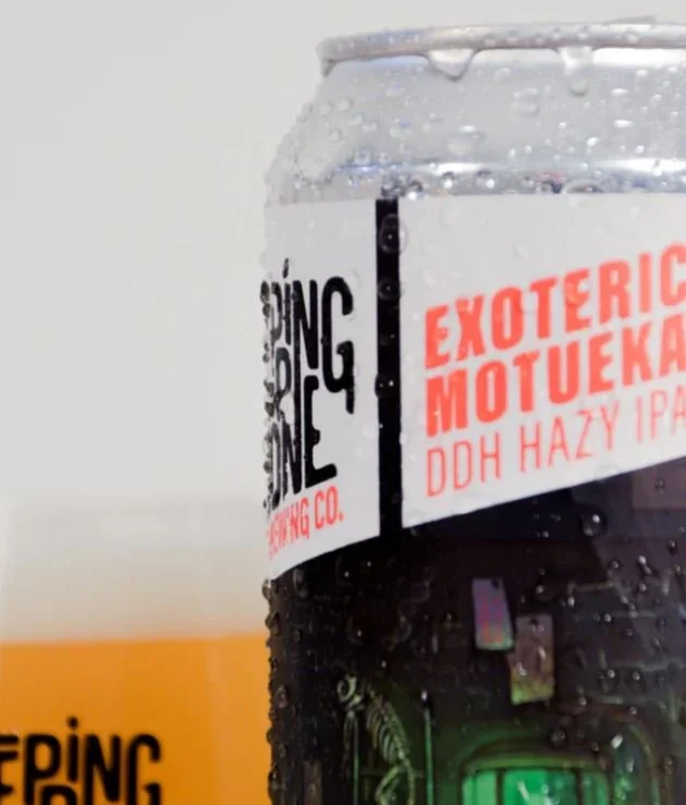 Close-up of a beer can with condensation, featuring bold black and orange text, partially showing the brand name and flavor.