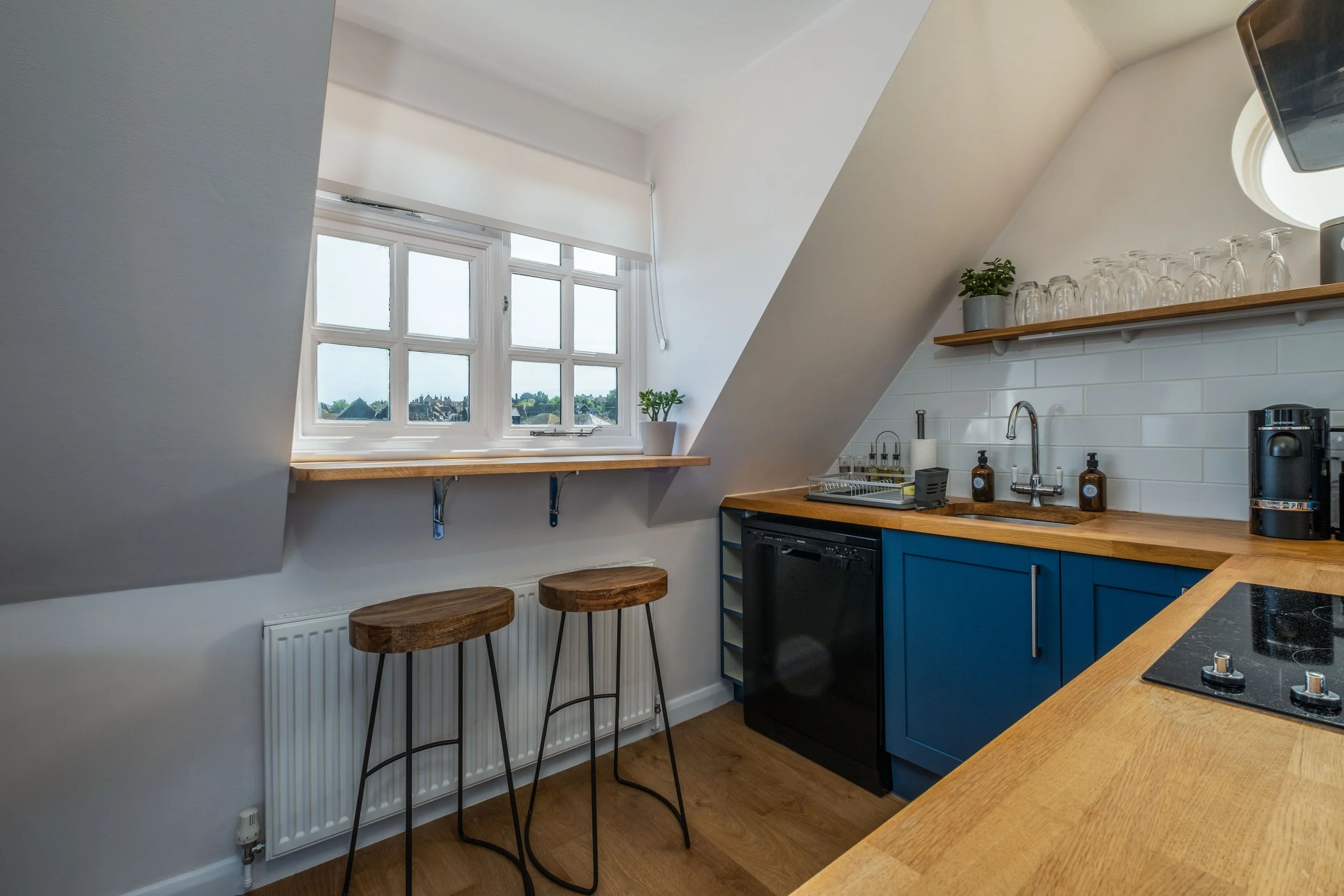 Kitchen with a window, blue cabinets, wooden countertop, a sink, and two barstools by the window.
