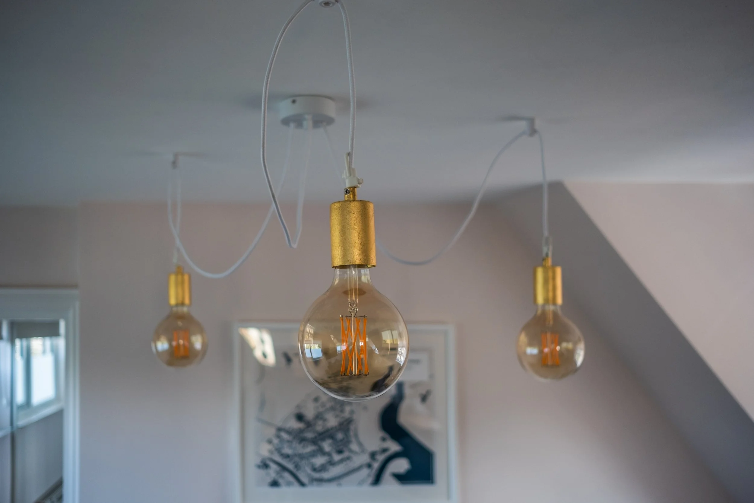 Three hanging Edison-style light bulbs with exposed filaments and gold fixtures, hanging from white cords in a modern interior space.