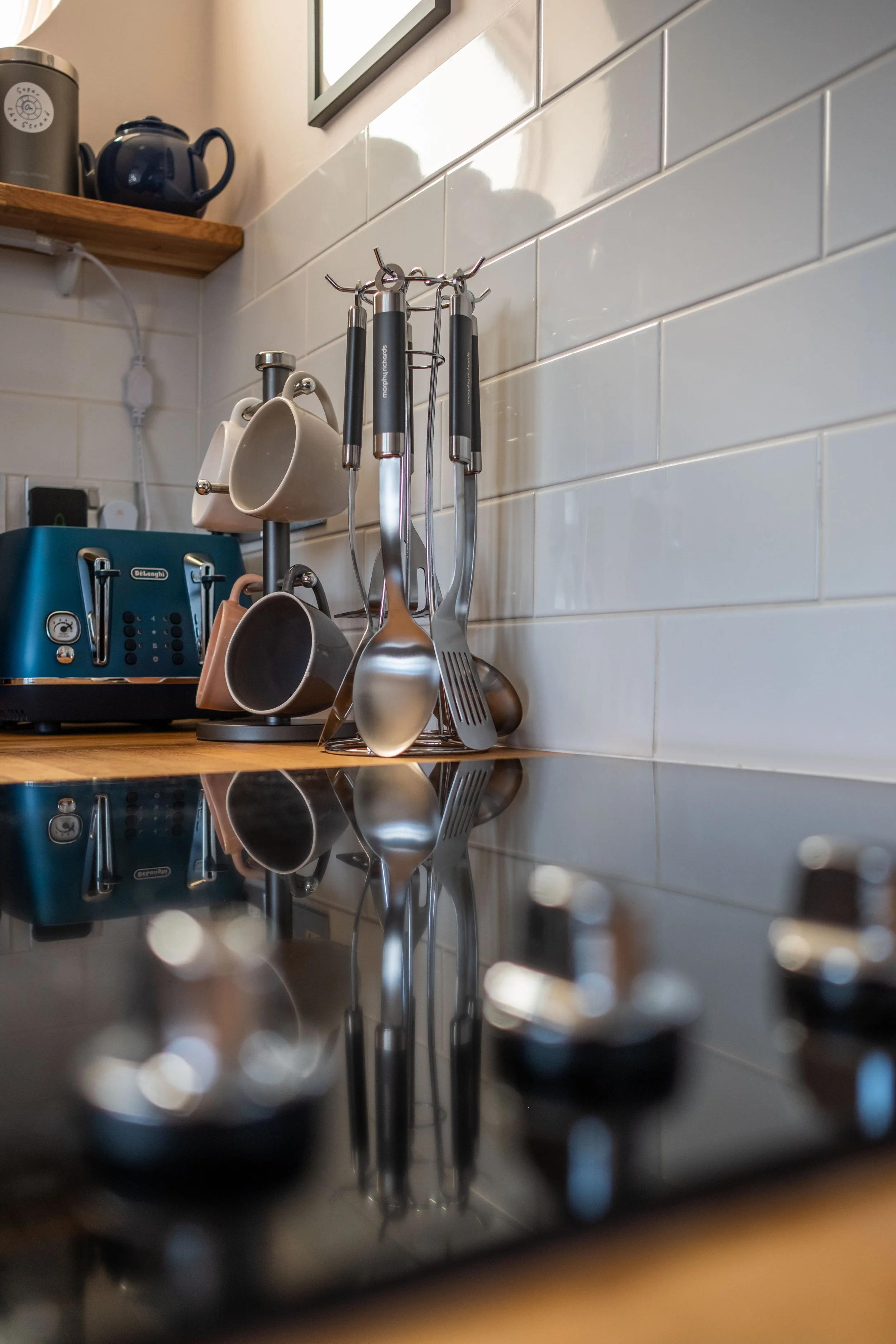Kitchen countertop with hanging utensils, mugs, and a blue toaster against a white subway tile wall.