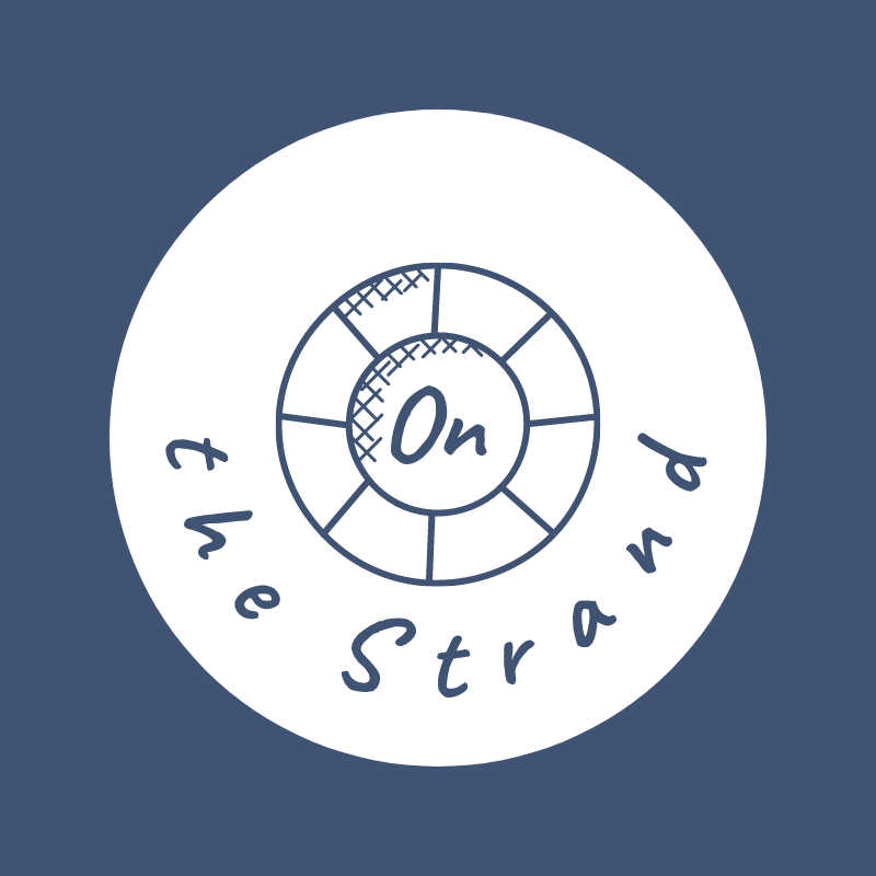 A graphic with a circular design and the text 'On the Strand' arched around the circumference. Inside, there is a smaller circle with a dial or gauge, featuring an 'On' indicator at the center.
