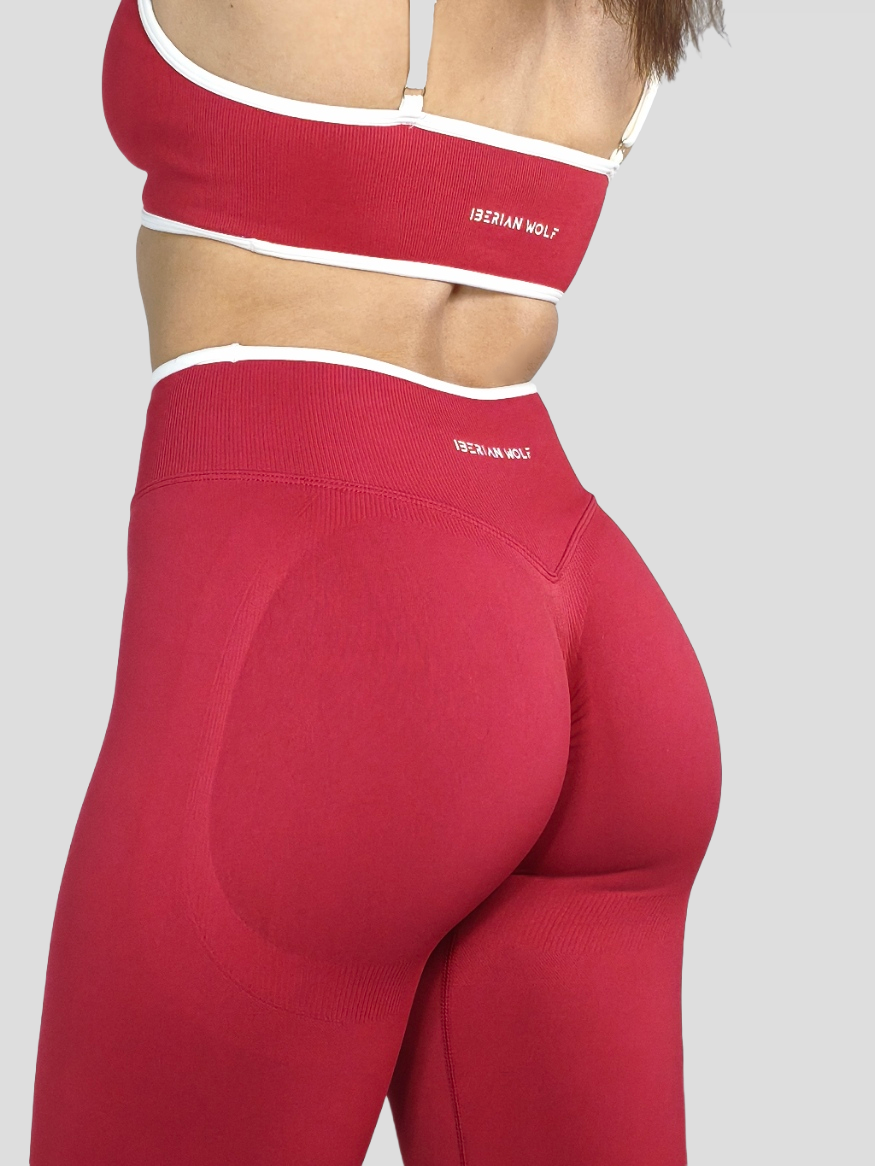Close-up of a woman's backside wearing red athletic leggings and a matching sports bra with white trim, displaying the brand name 'IBERIAN WOLF'.
