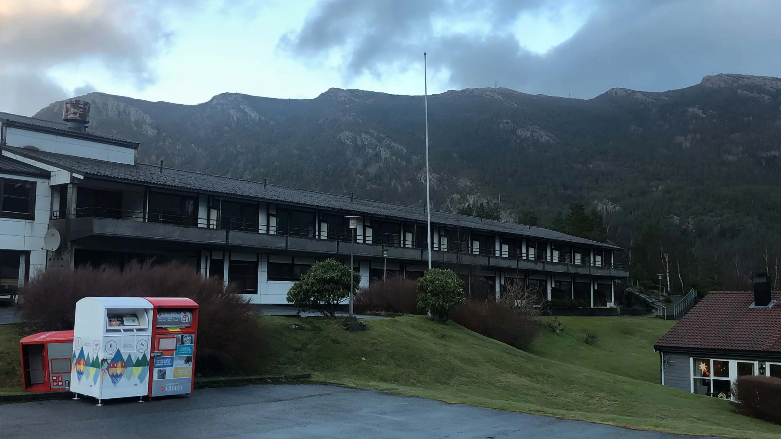 Bilde av en boligblokk foran fjell med tåkete himmel og skylag i bakgrunnen.