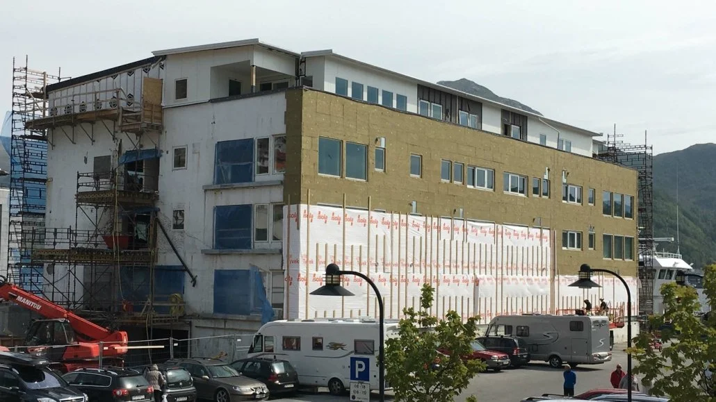 Bygning under oppføring med scaffolding og en parkeringsplass foran