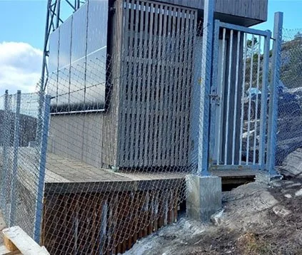 En grå metallport og gjerde ved en bygning på en skrånende jordflate.