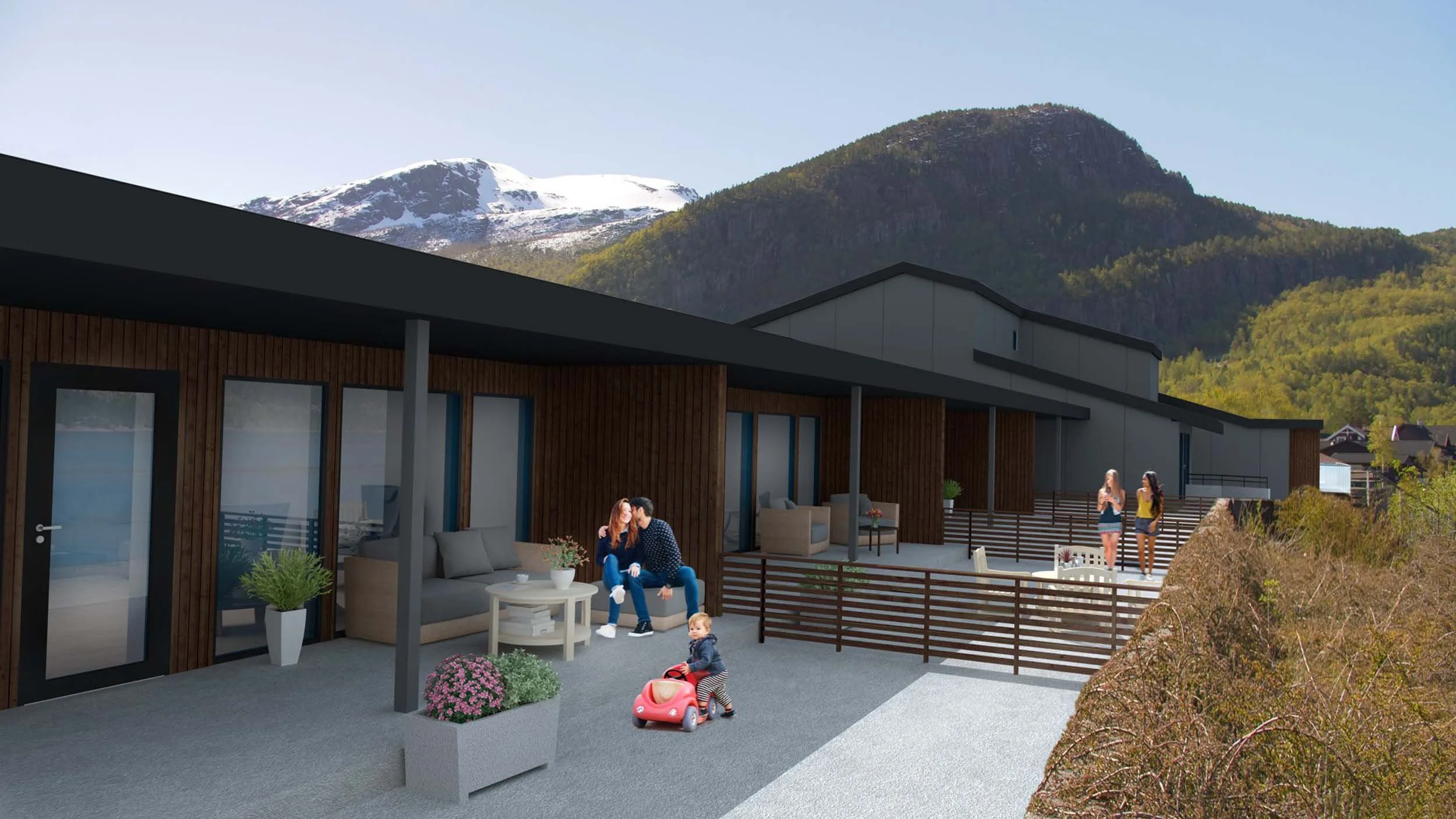 Familie på terrassen til en moderne bygning med utsikt mot fjell og snødekte topper.
