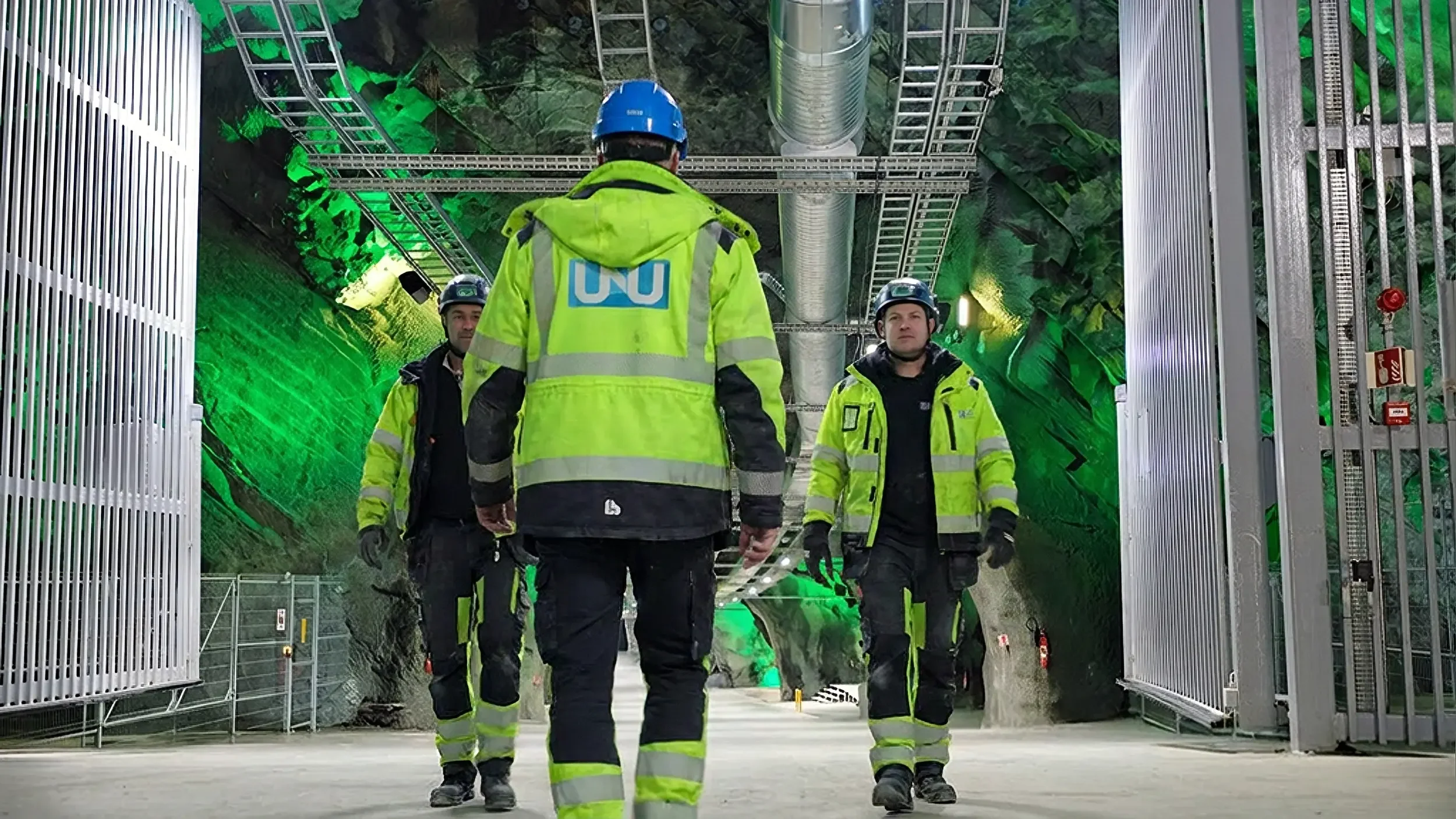 Firemenn i gult og blå hjelmer i en underjordisk tunnel med grønn belysning.