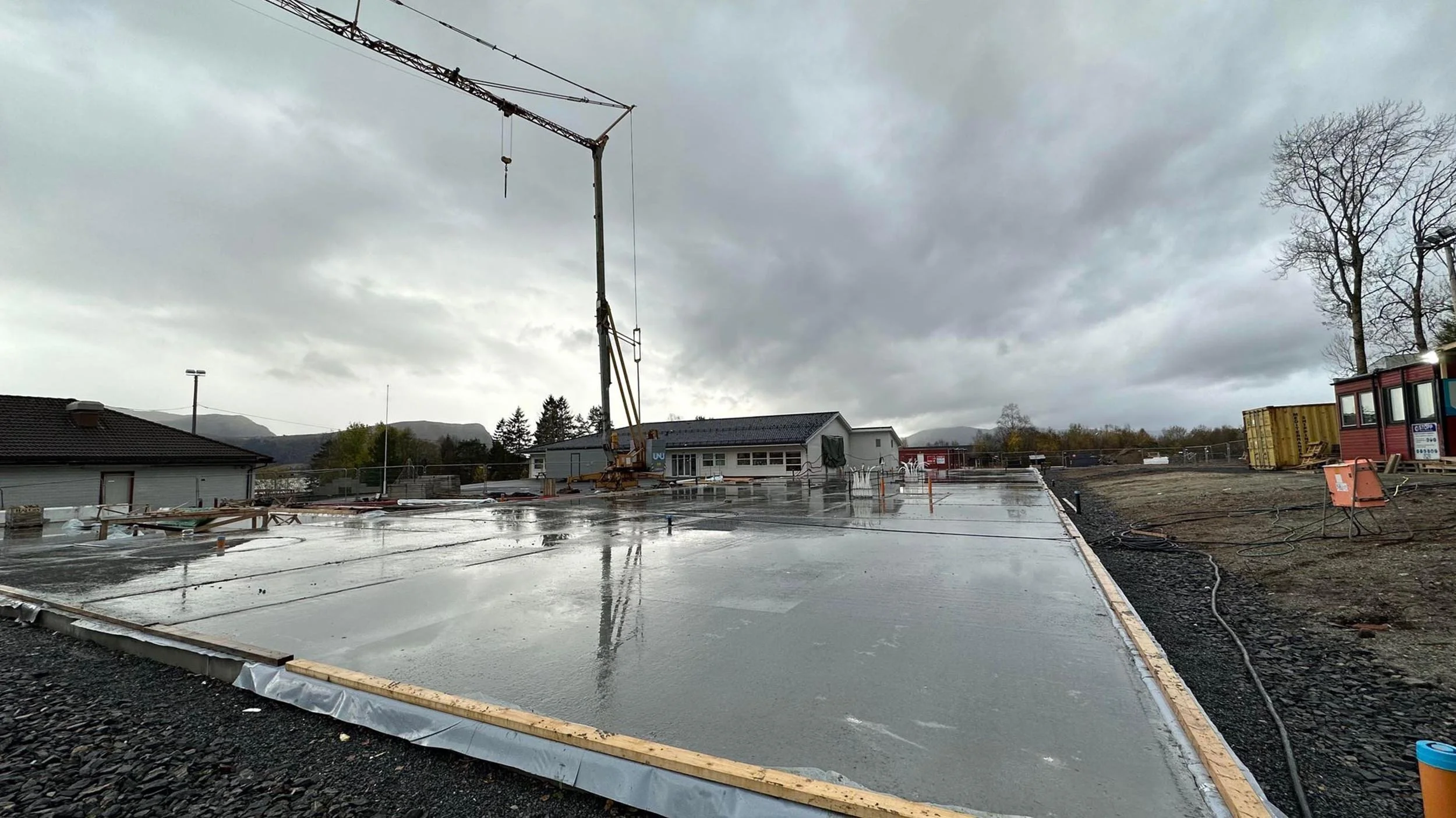 Byggeplass med nylagt støpt betonggulv, byggeutstyr, og et overskyet vær