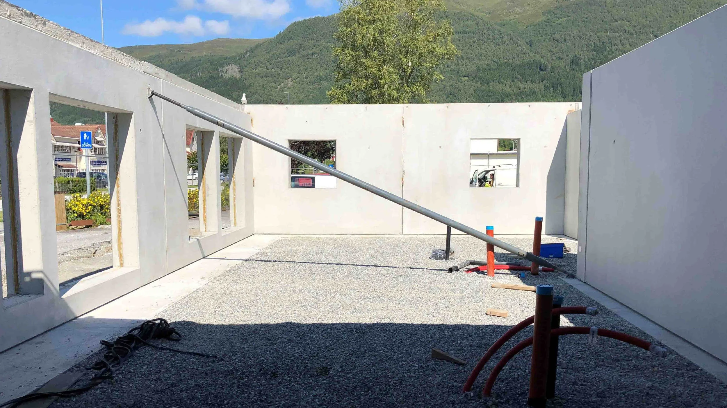 Byggefase med vegger under oppføring, med vinduer, og utstyr for bygging. Bakgrunn med fjell og blå himmel.