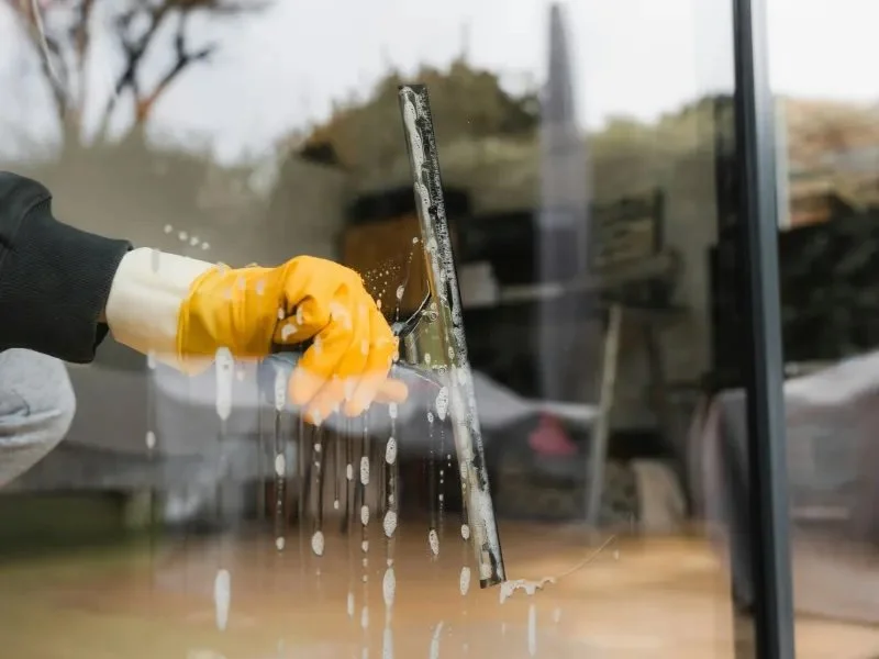 Person cleaning a glass window with a squeegee, wearing yellow rubber gloves.