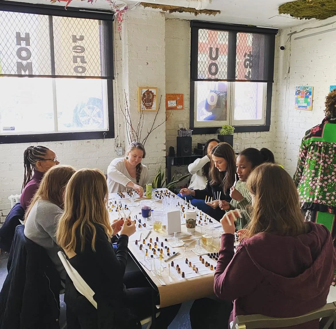 A group of women playing chess at a long table inside a room with white brick walls and large windows.
