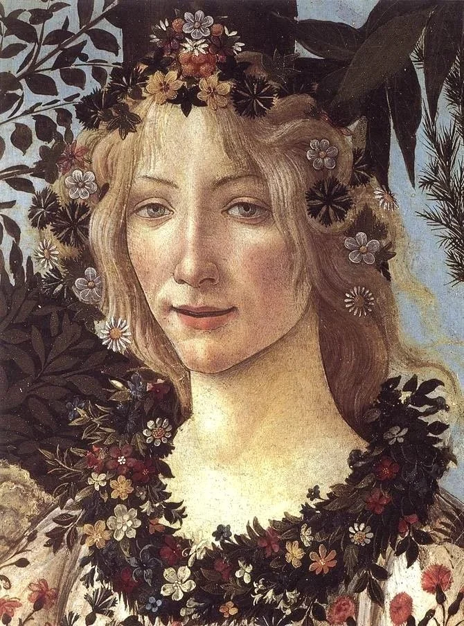A woman with long, wavy hair surrounded by flowers and dark leaves, with light-colored skin and a gentle expression.
