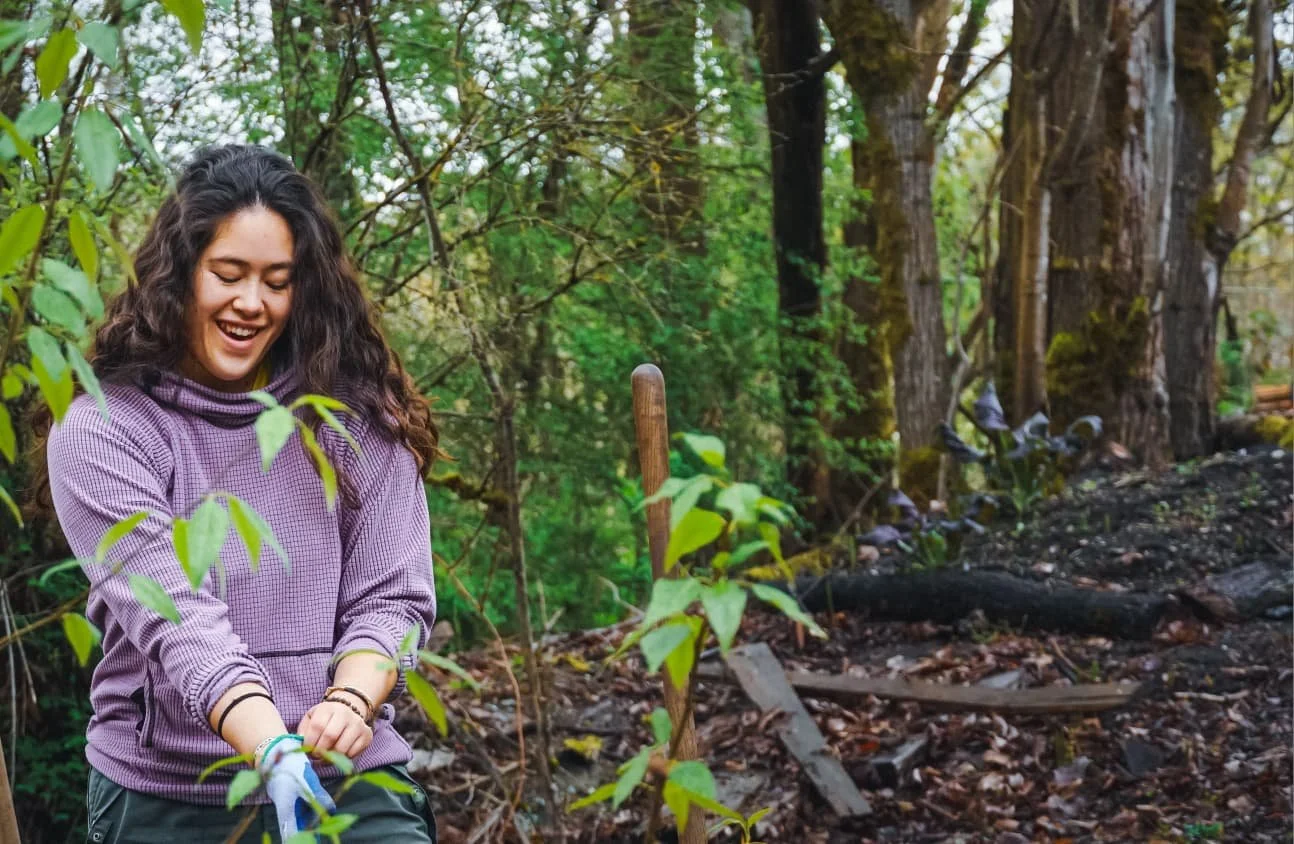 Tatiana Brown at Heron's Nest, near the Duwamish Longhouse, planting a small tree in a forested area.