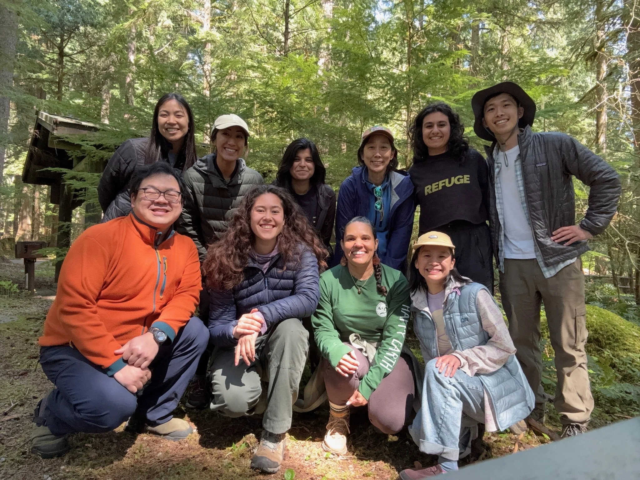 Group of people smiling and posing for a photo in a forest with green trees in the background.