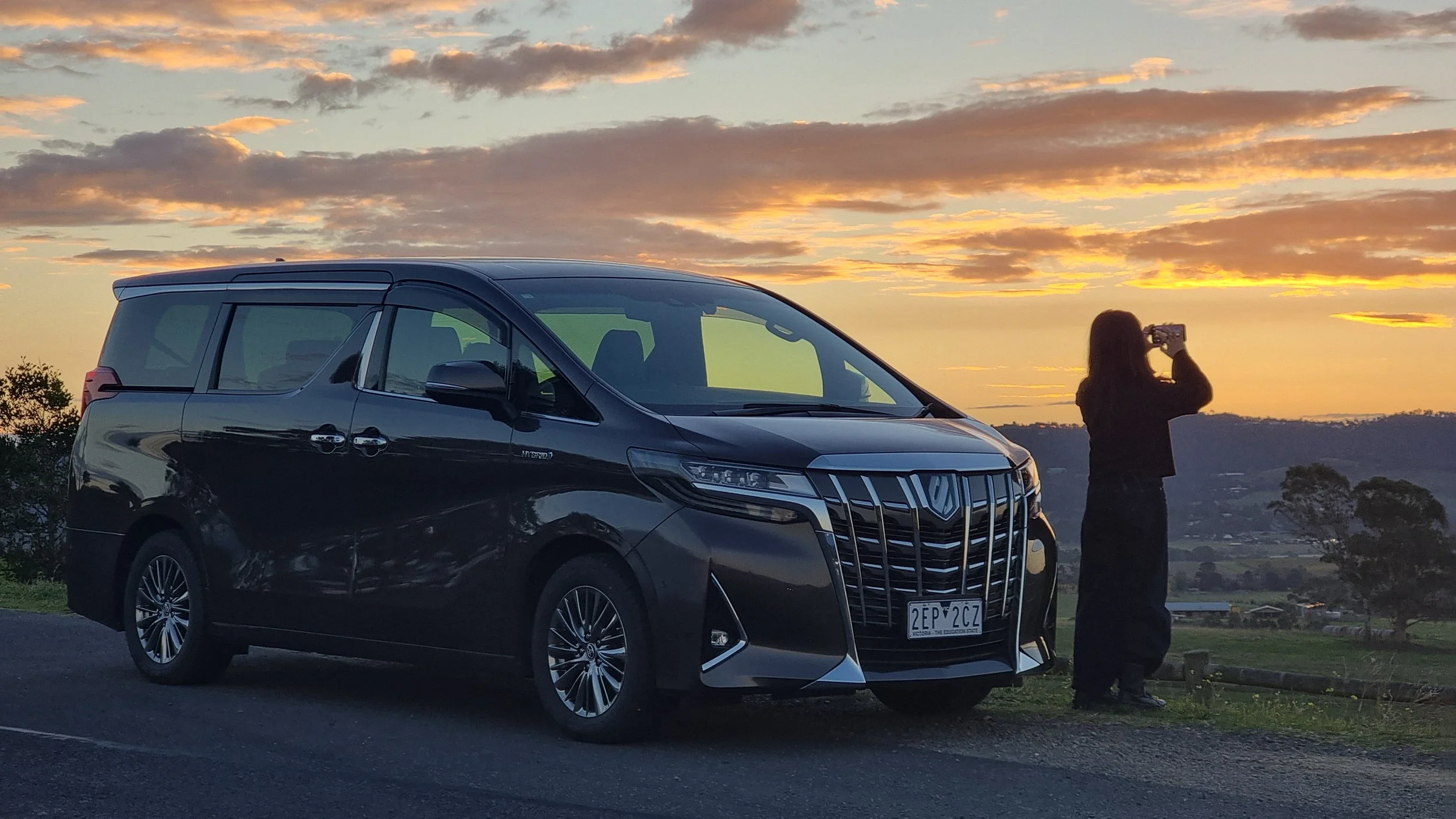 黒い車と女性が夕焼けの空の前で写真を撮っている風景