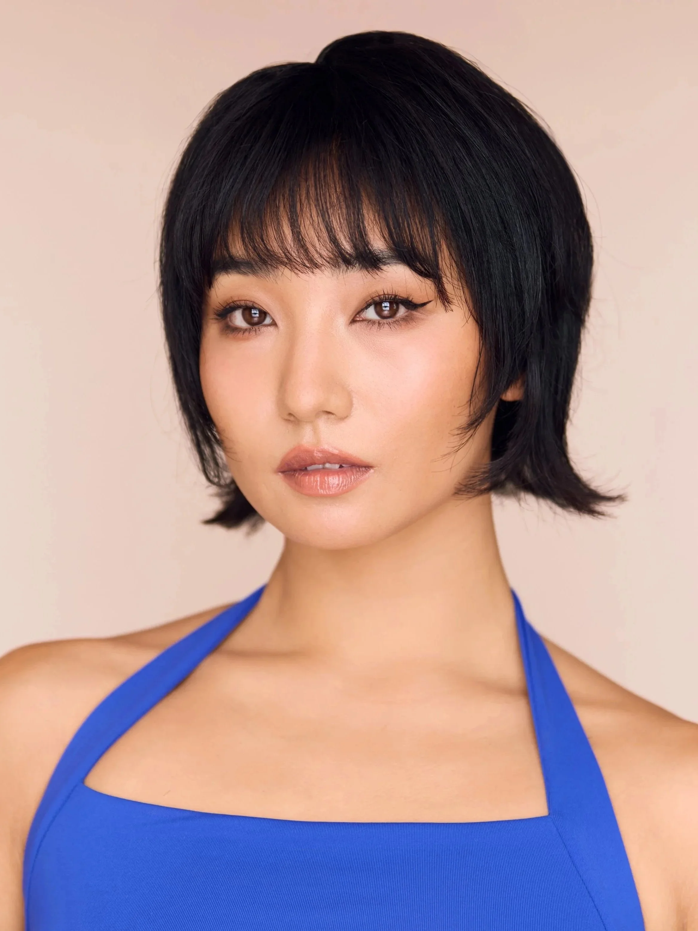 Close-up of a woman with short black hair, brown eyes, and wearing a blue top with straps.