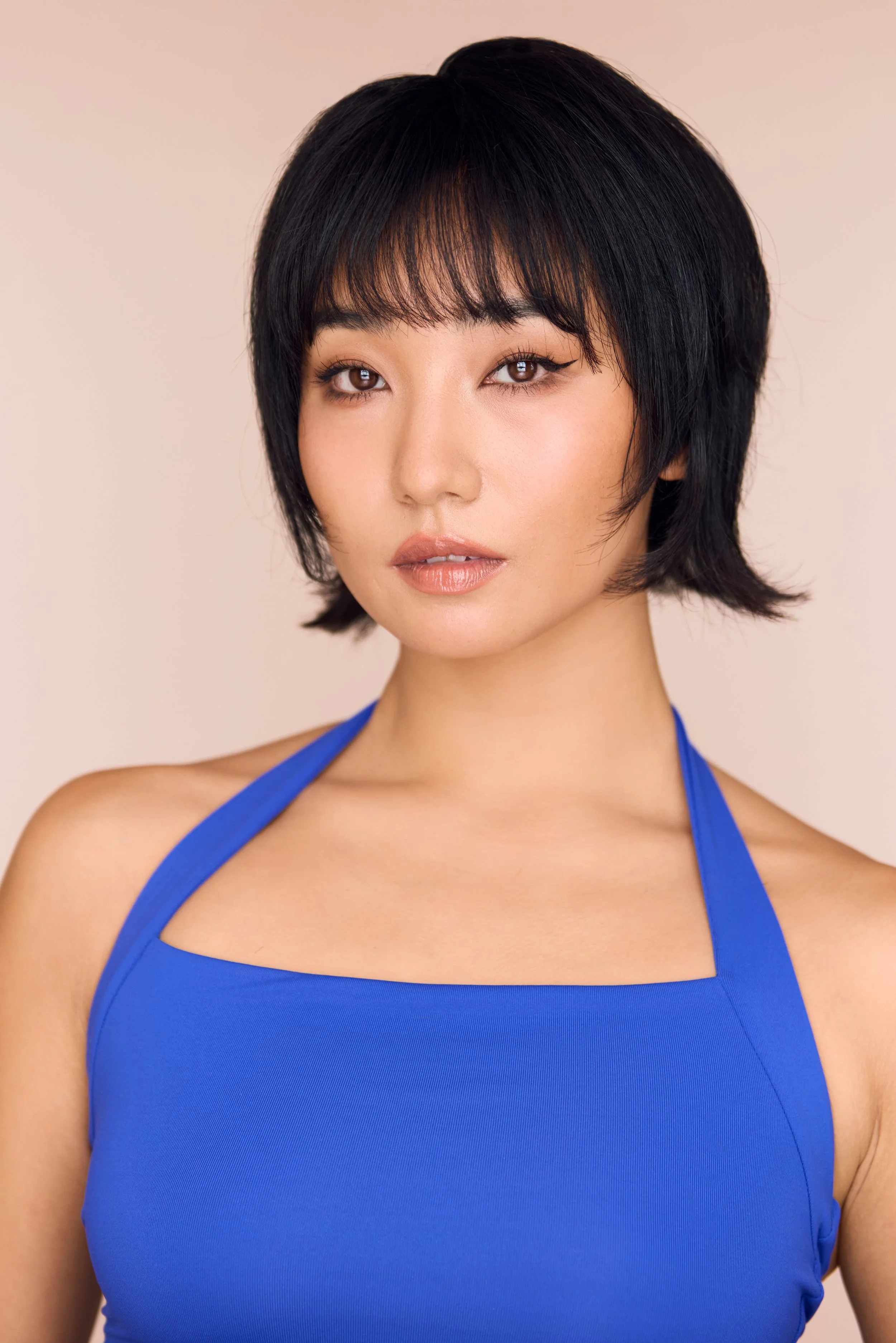 Close-up portrait of a young woman with short black hair wearing a blue halter top, against a neutral background.
