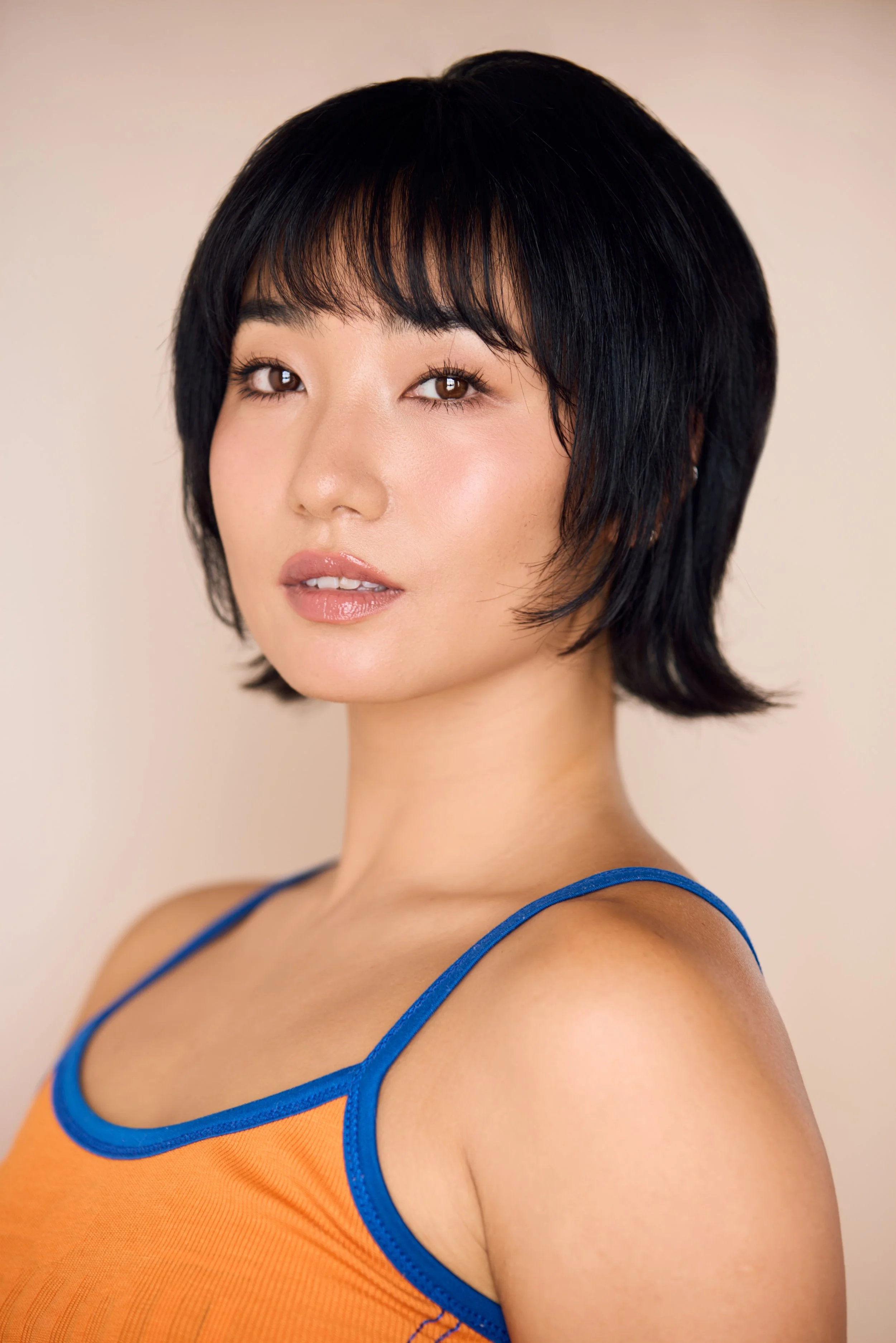 A woman with short black hair and light makeup wearing a blue and orange athletic tank top, looking slightly to the side, against a neutral background.