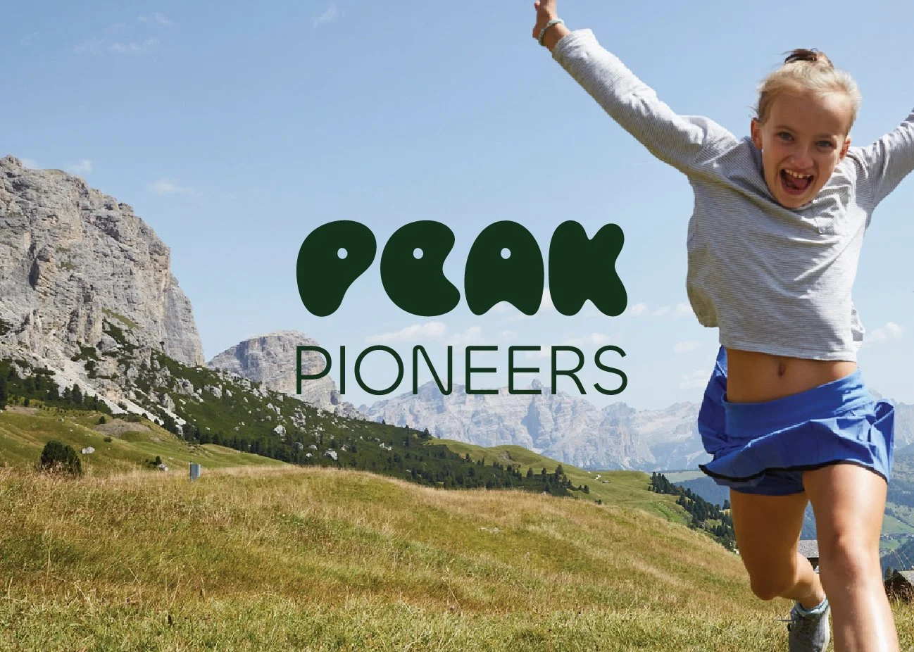 A young girl running joyfully in a grassy mountain landscape with cliffs in the background, and the words 'Peak Pioneers' overlayed on the image.