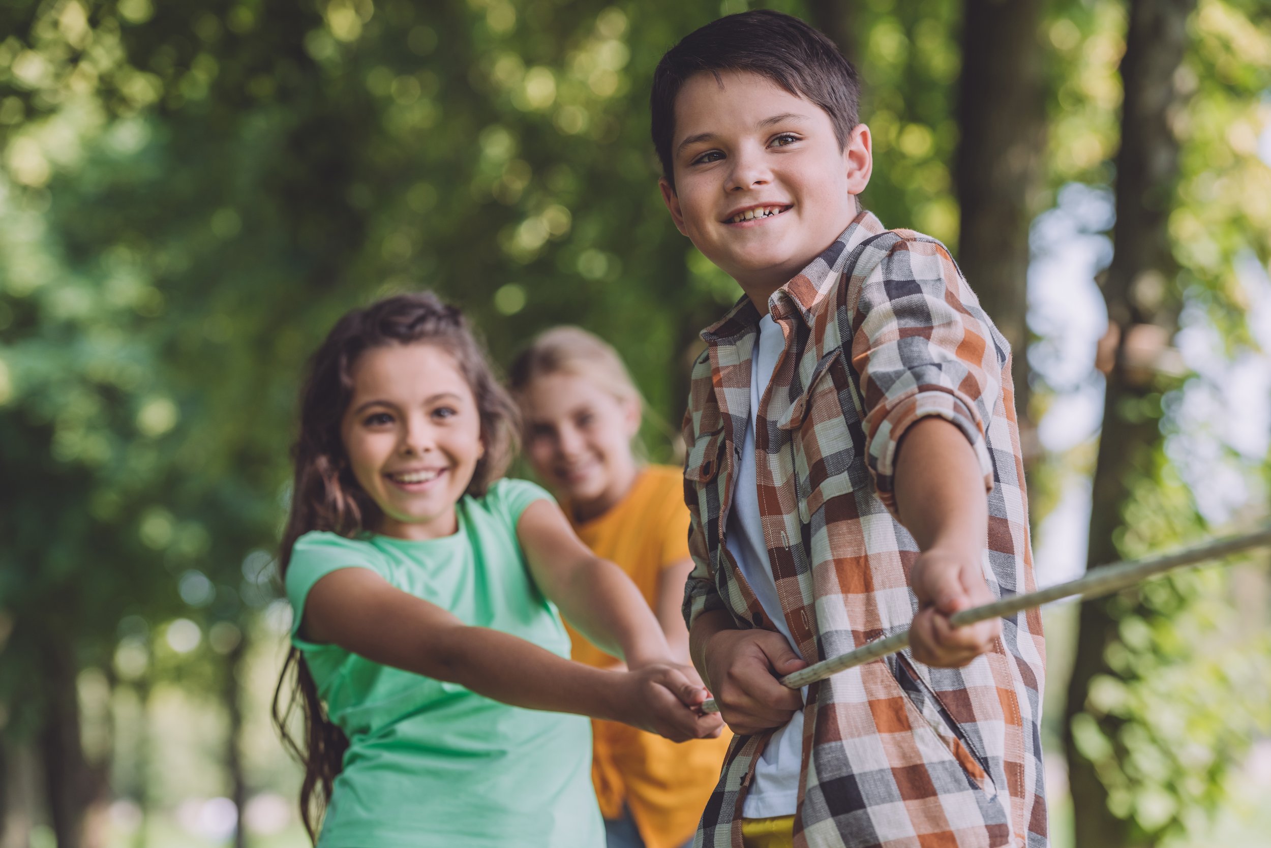 Group of children on a swing in a park, smiling and holding hands, with green trees in the background.