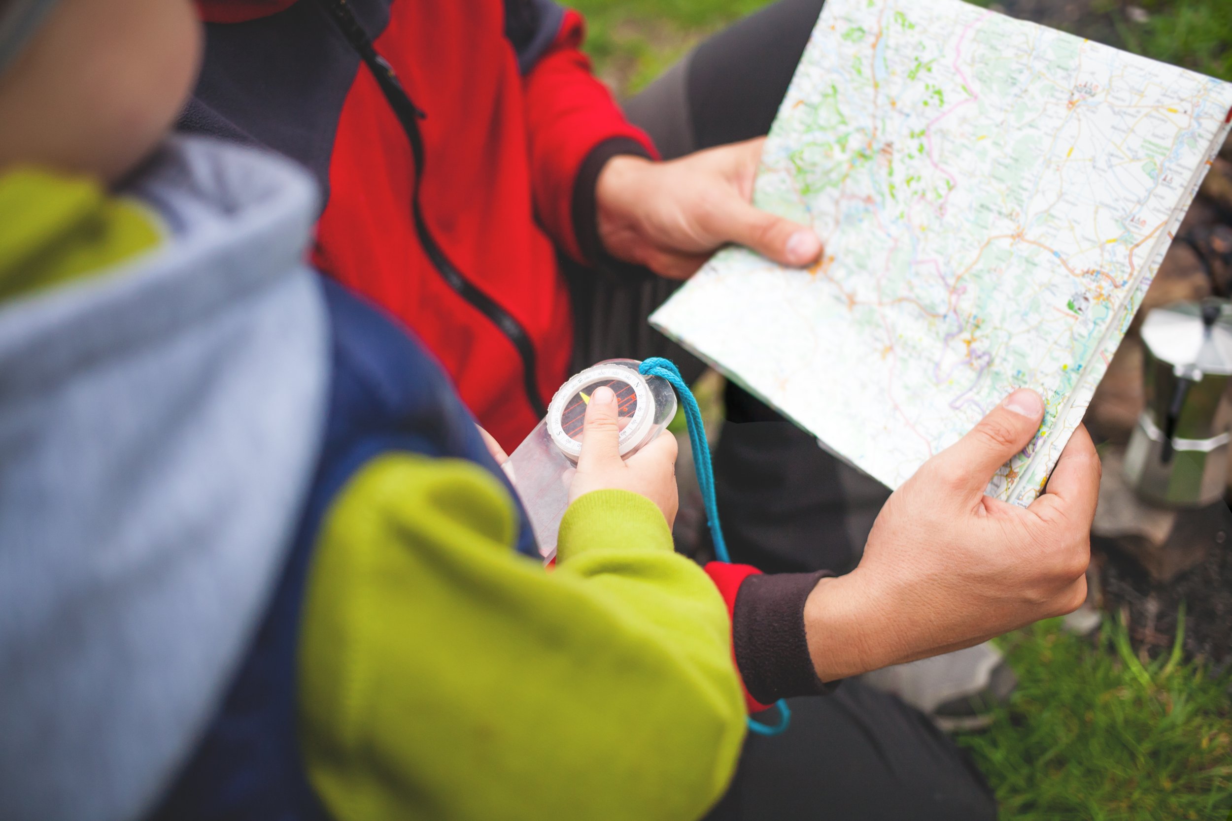 Two individuals holding a detailed topographic map outdoors, with one person pointing to a location on the map and the other holding a compass.