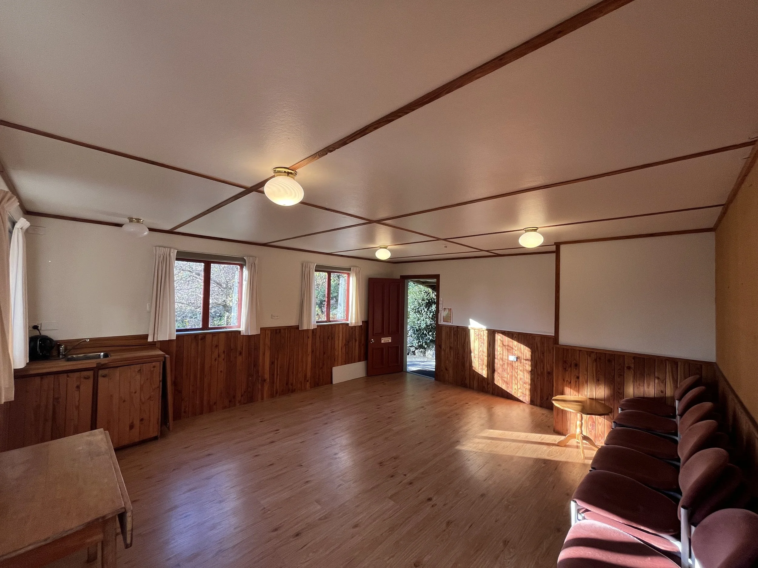 Interior of a room with wooden accents, windows with curtains, and ceiling lights, featuring a row of brown upholstered chairs.