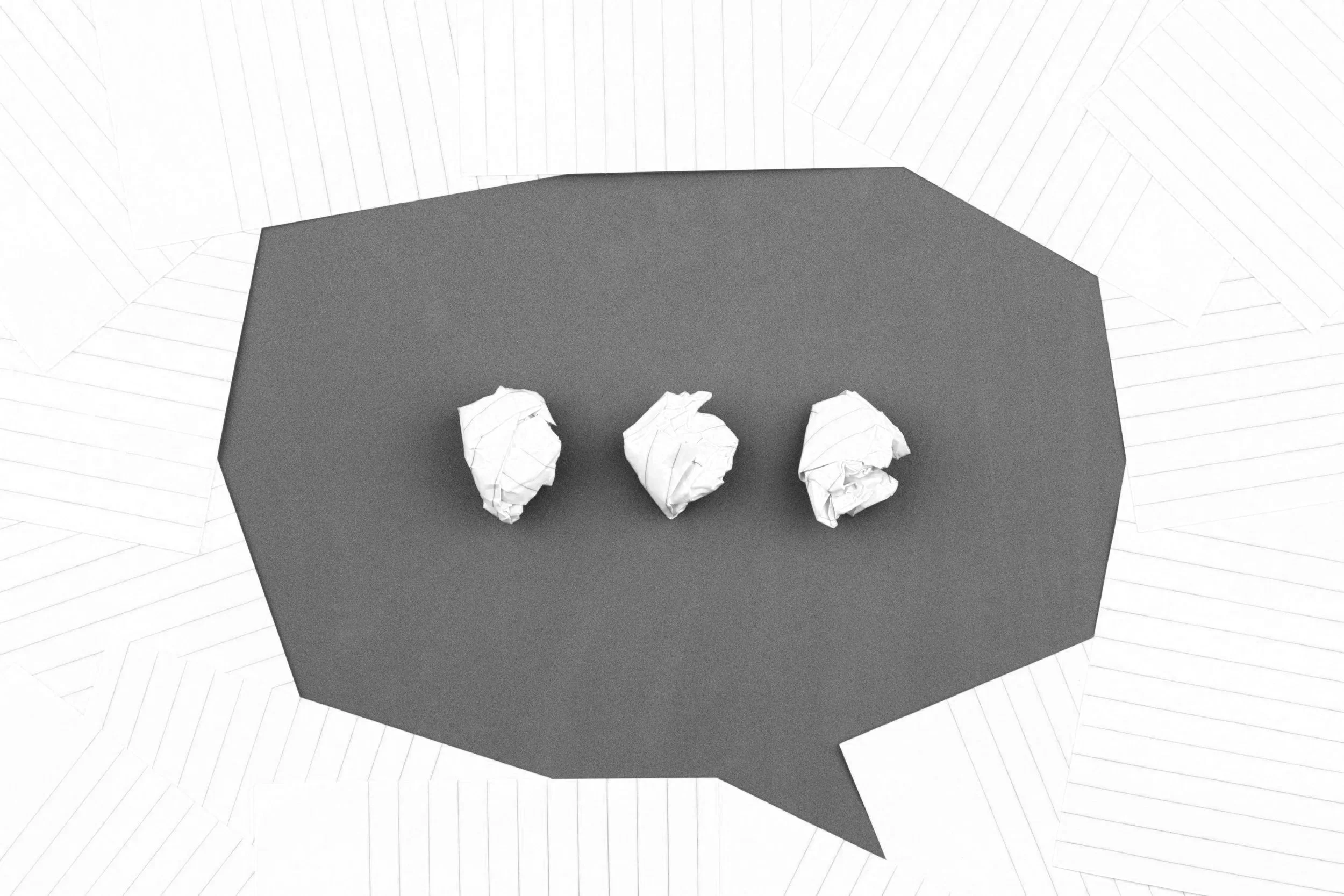 Three crumpled pieces of white paper on a dark tabletop with a textured surface, positioned in a row.
