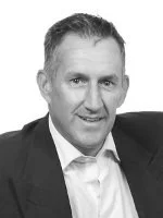 Black and white headshot of a smiling man in a suit and white shirt.