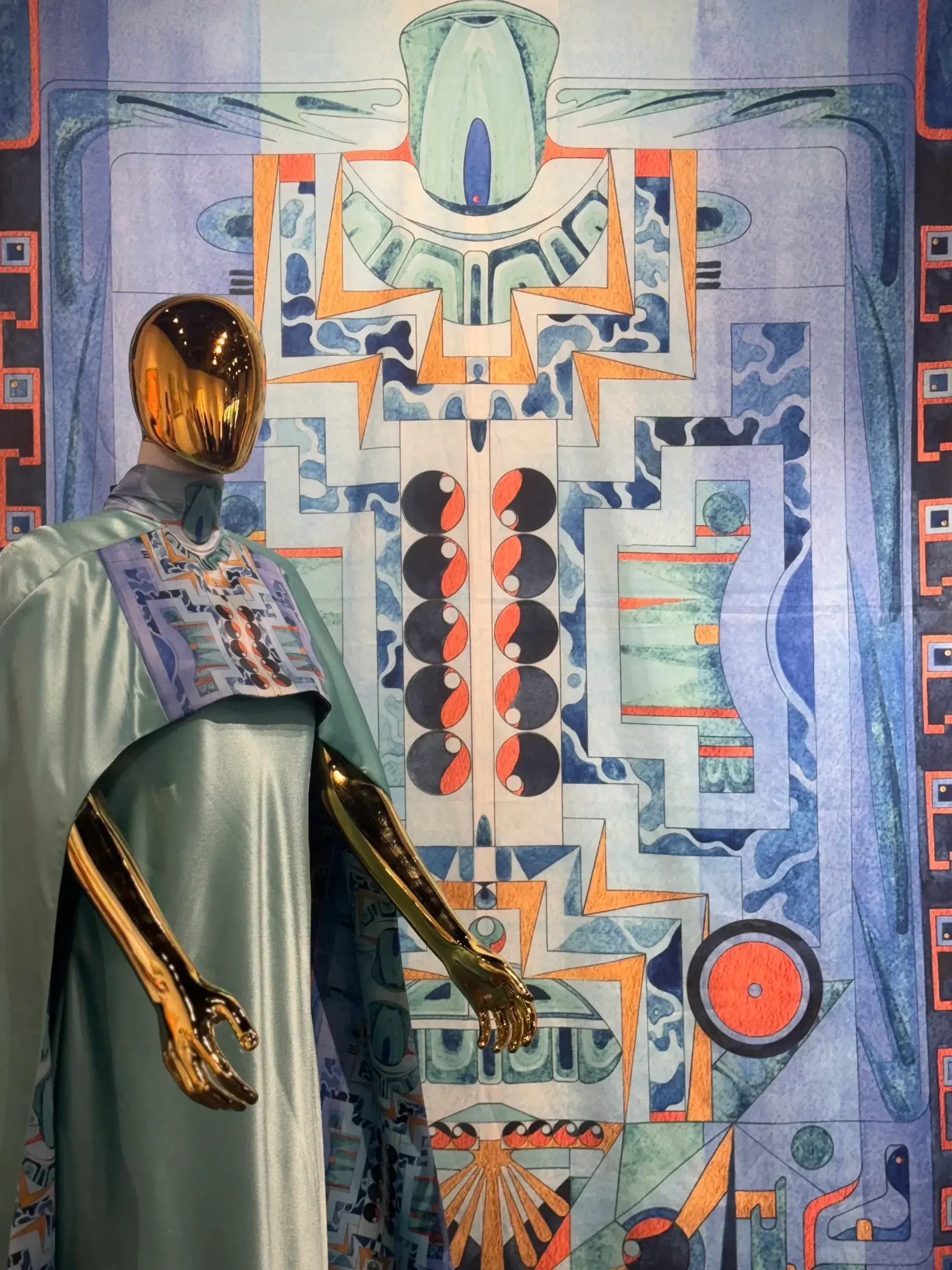 A mannequin dressed in the gown stands in front of a large fabric hanging of the artwork. 