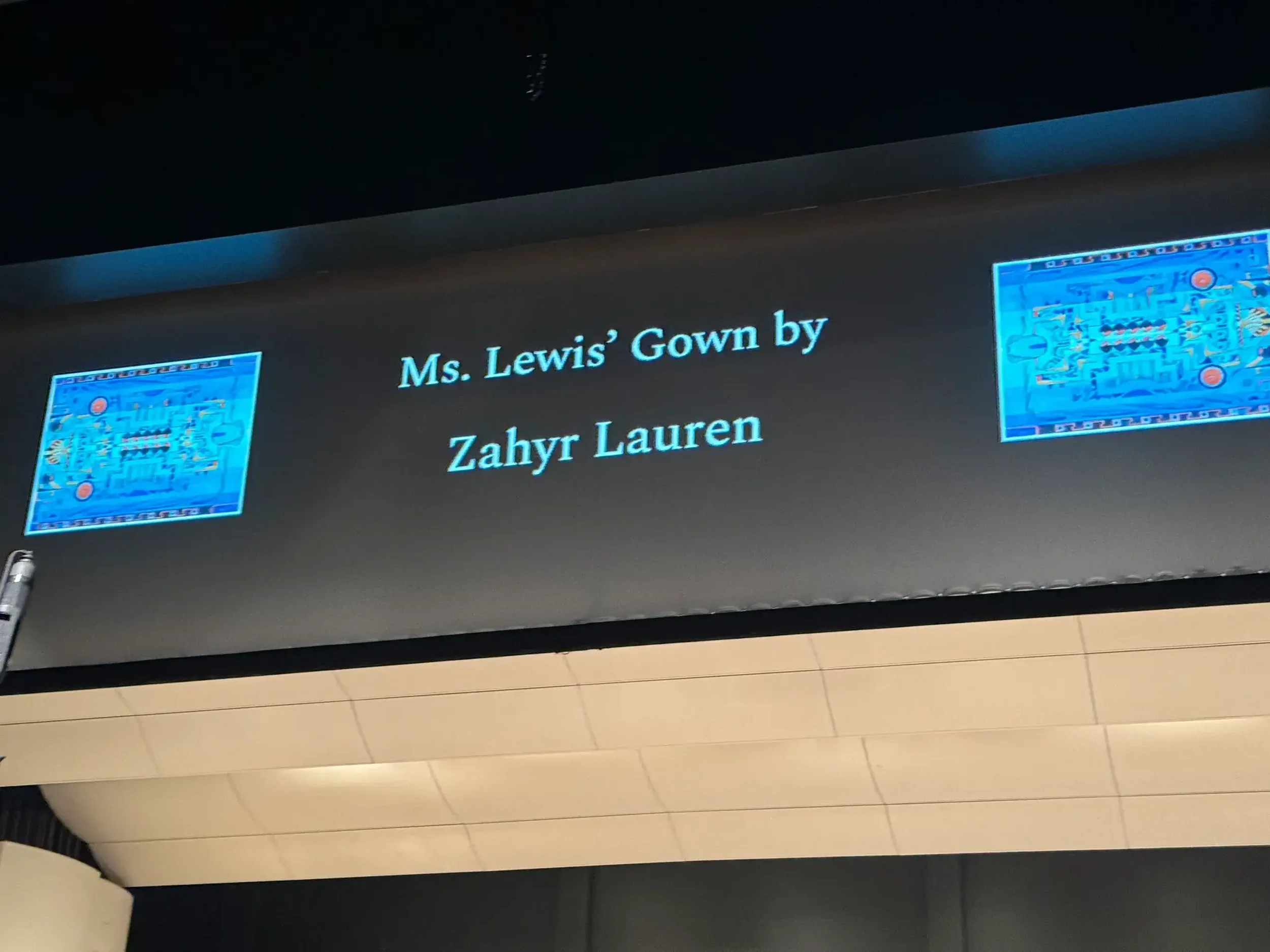 Video screen at the performance, showing the text “Ms. Lewis’ Gown by Zahyr Lauren”.