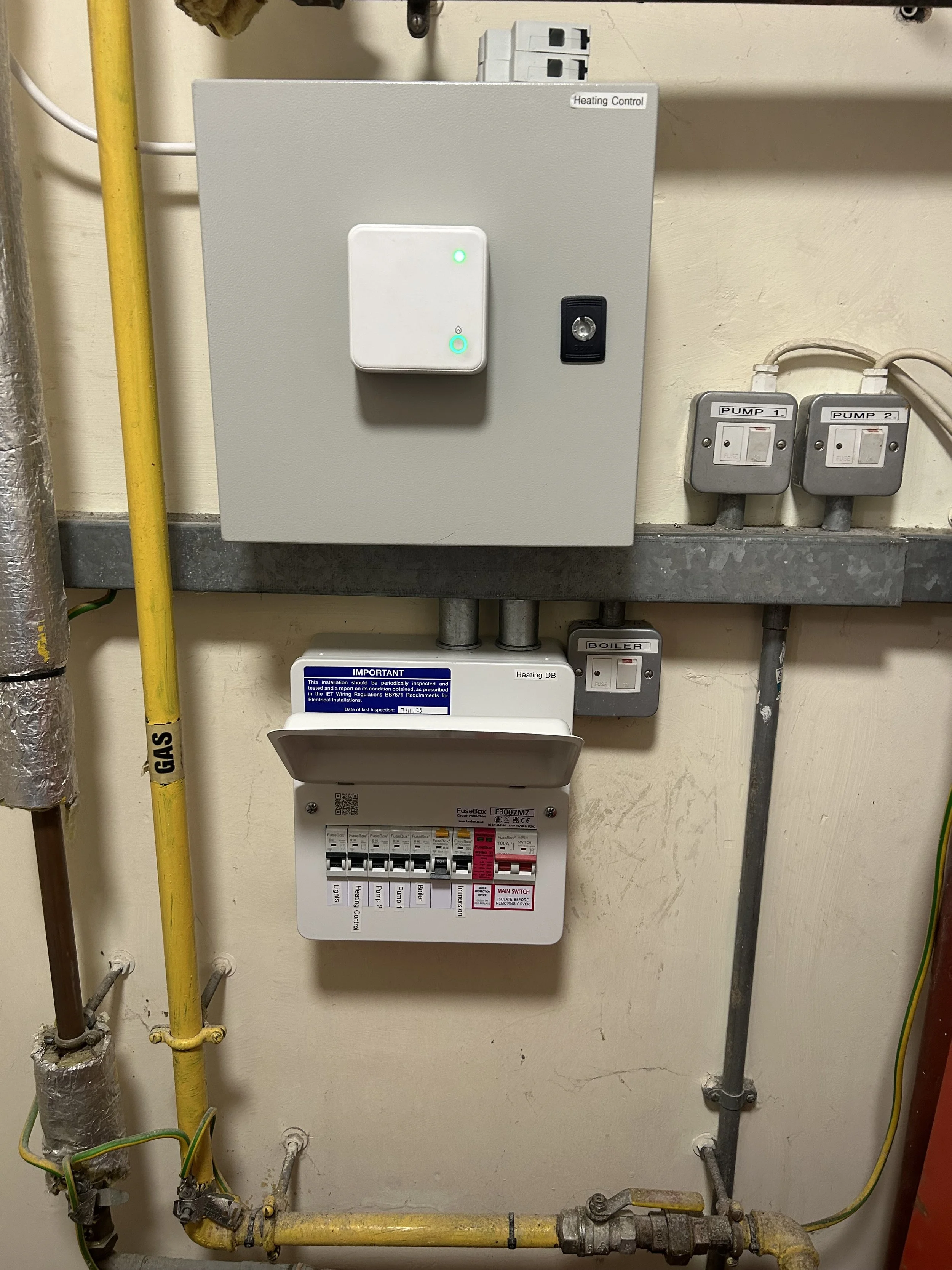 Electrical and control panel with wiring, switches, and labeled components for heating and pumping systems in a mechanical room.