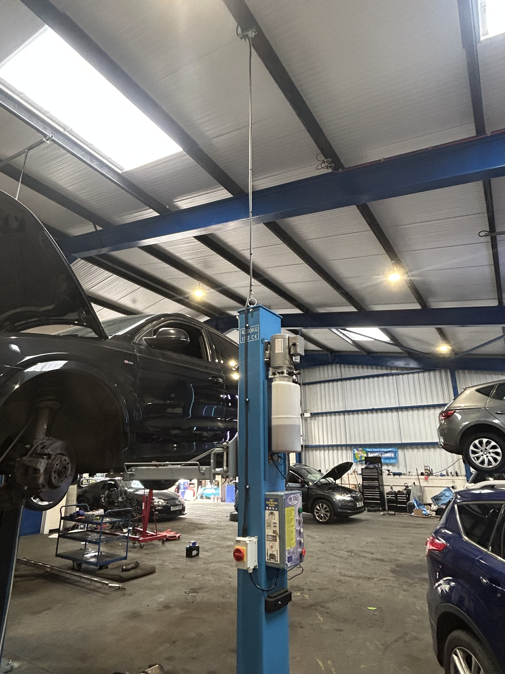 Interior view of an auto repair shop with a black car on a lift, a gray car on the ground, and tools and equipment scattered around.