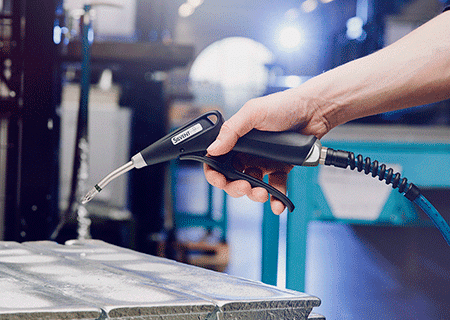 A person is holding a soldering iron above a circuit board in a workshop setting.