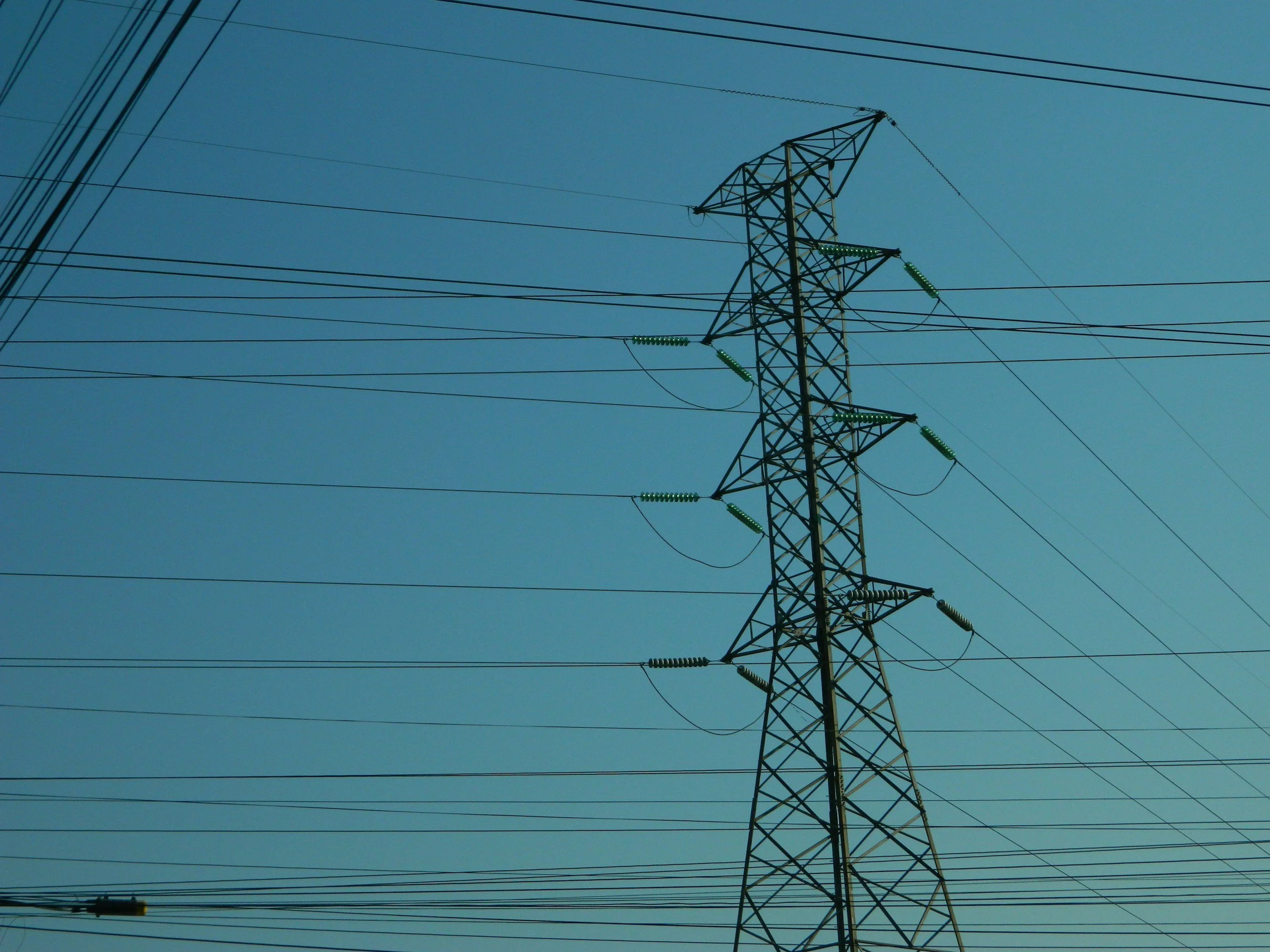 A tall electrical power line tower with multiple power lines extending from it against a clear blue sky.